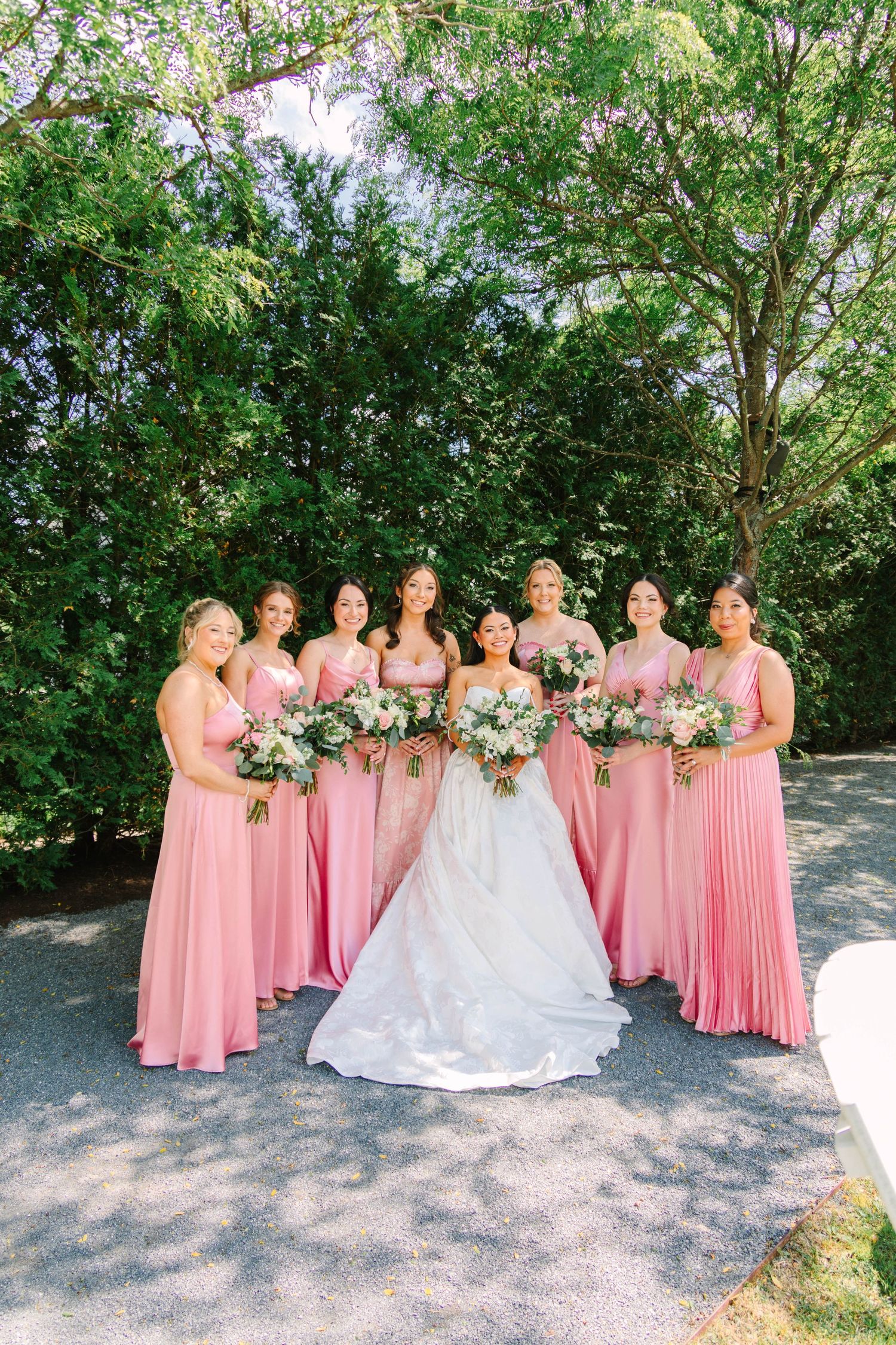 Bride in white ballgown posing with seven bridesmaids in pink dresses holding floral bouquets.