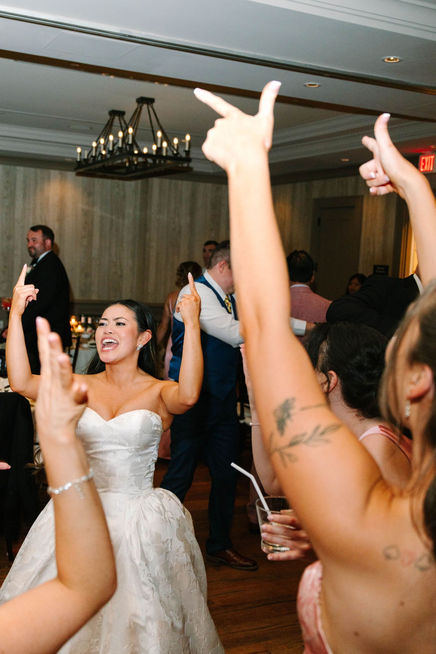 Bride singing and dancing with hands raised by guests at wedding reception celebration.