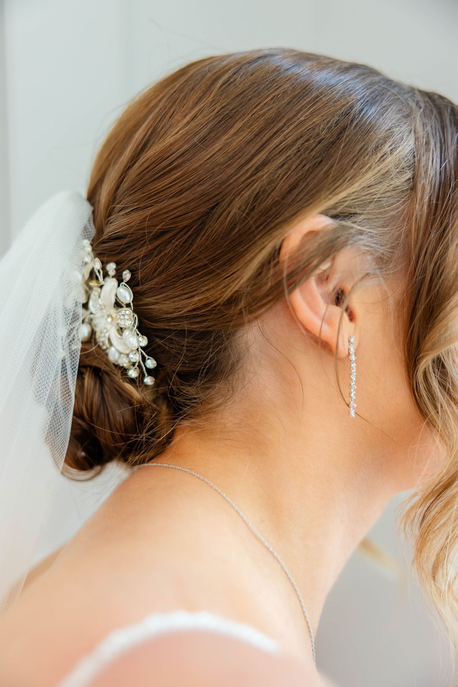 Close-up of bride's elegant updo with pearl floral hair accessory, veil, and diamond drop earring.