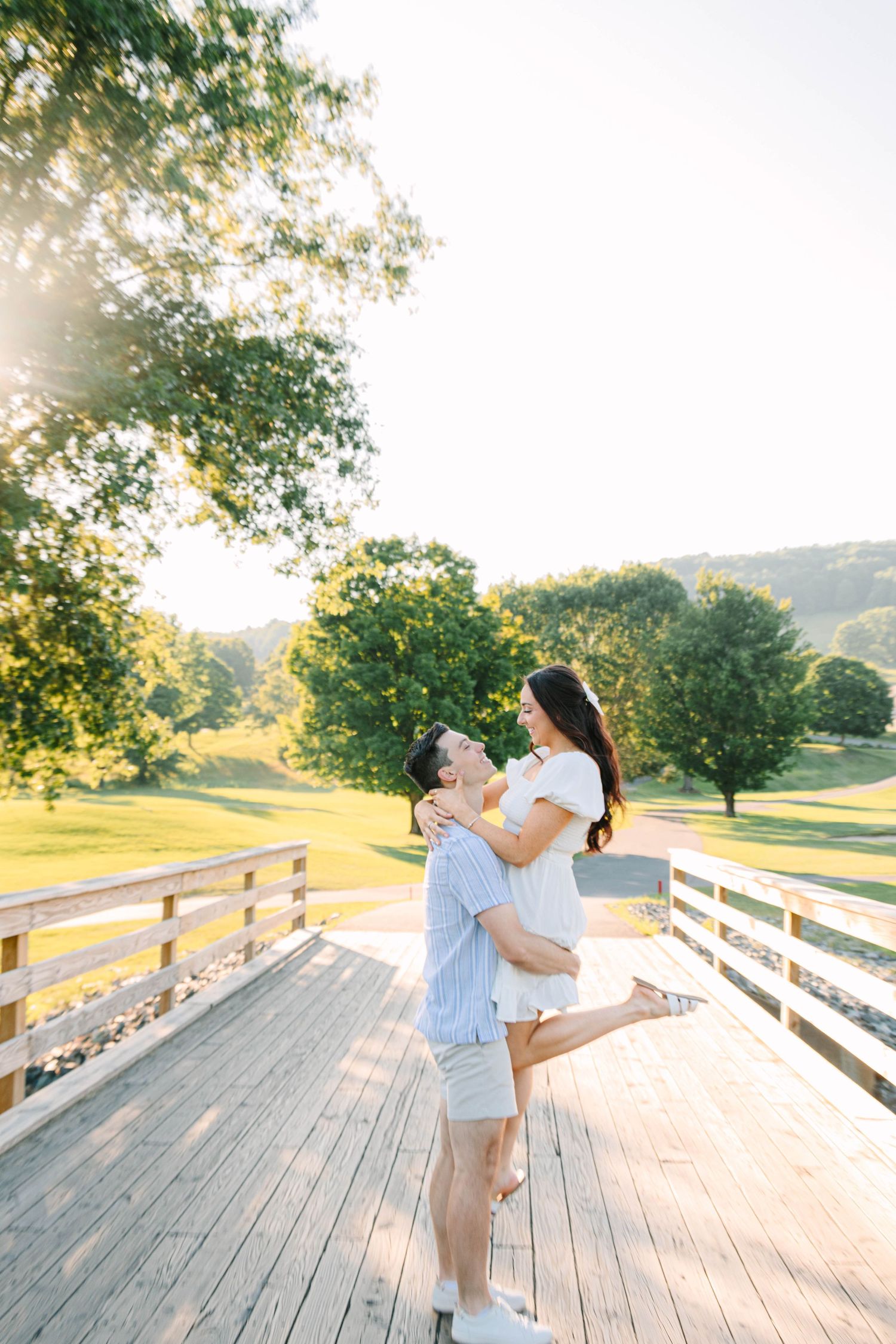 Couple embracing on a wooden bridge at golden hour in a lush green park.