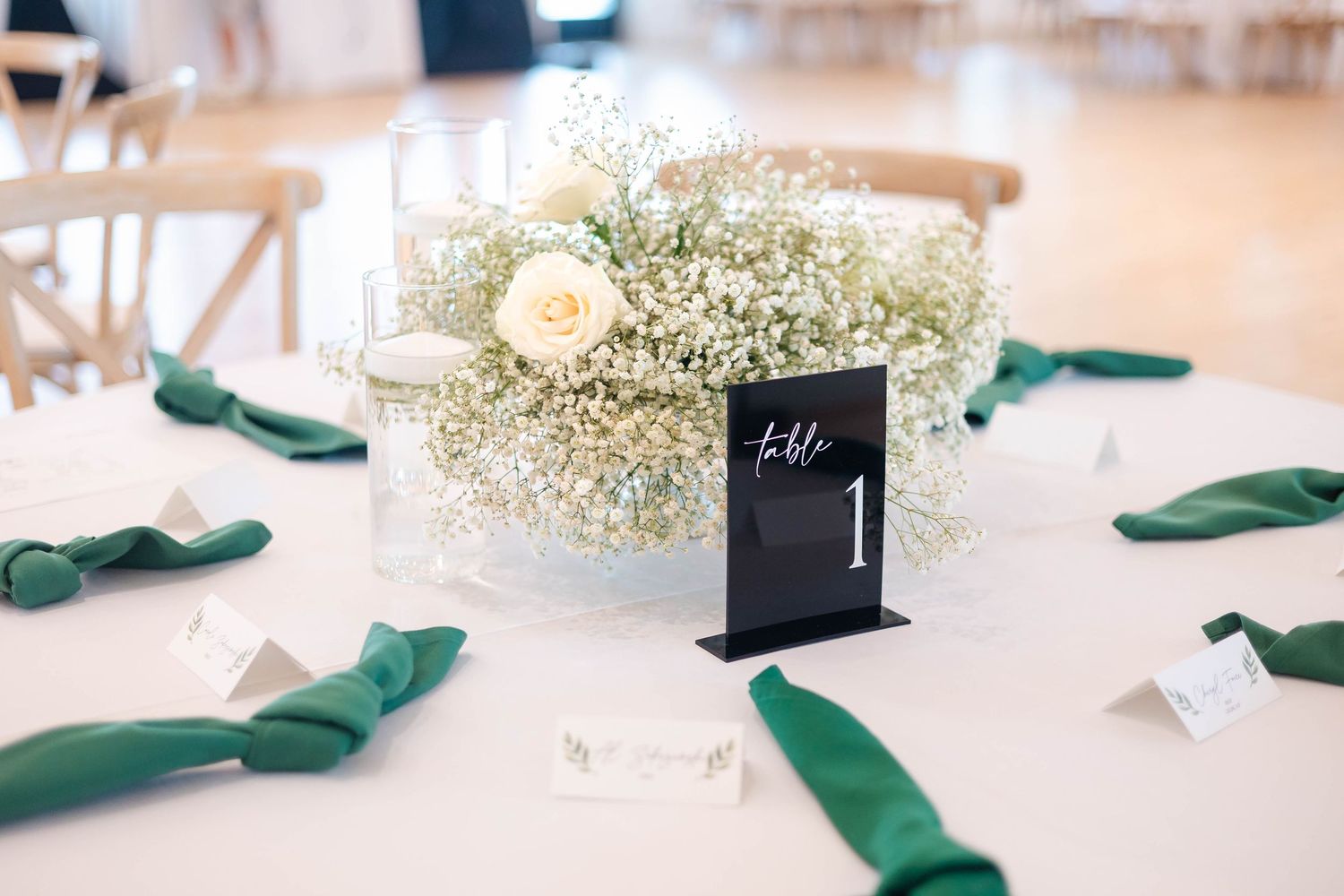 Elegant wedding table centerpiece with baby's breath, white rose, green napkins, and table number card.