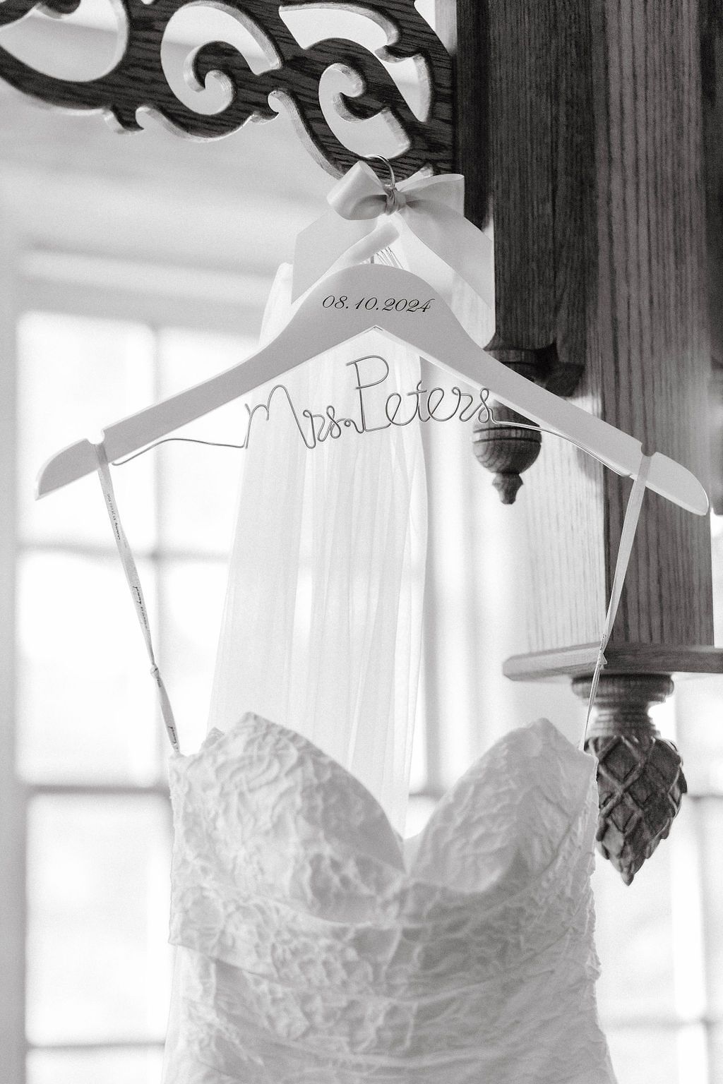 Black and white photo of a lace wedding dress on a custom Mrs. Peters hanger dated 08.10.2024.