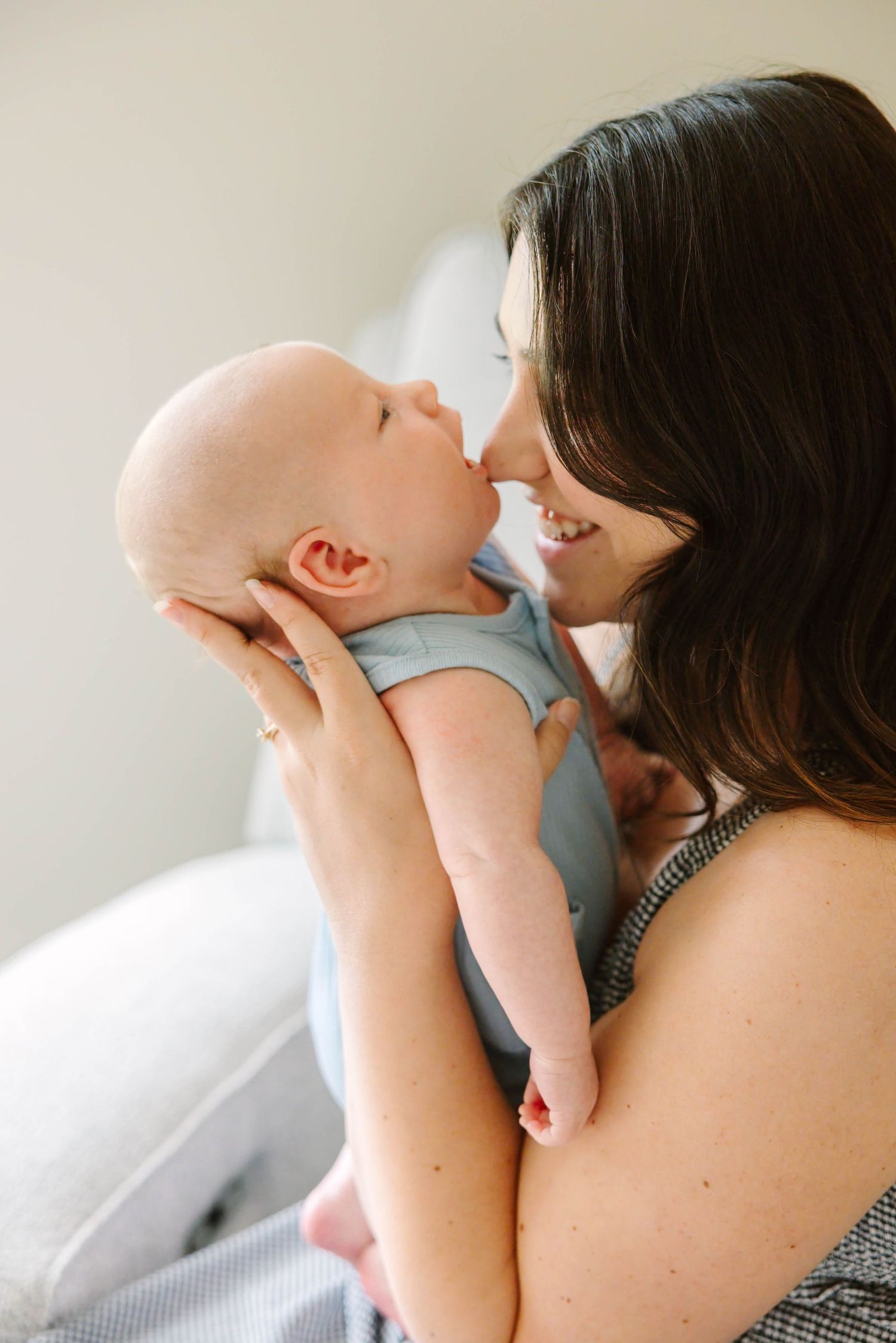 A smiling mother tenderly holds her newborn baby close, touching noses in an intimate and loving moment.