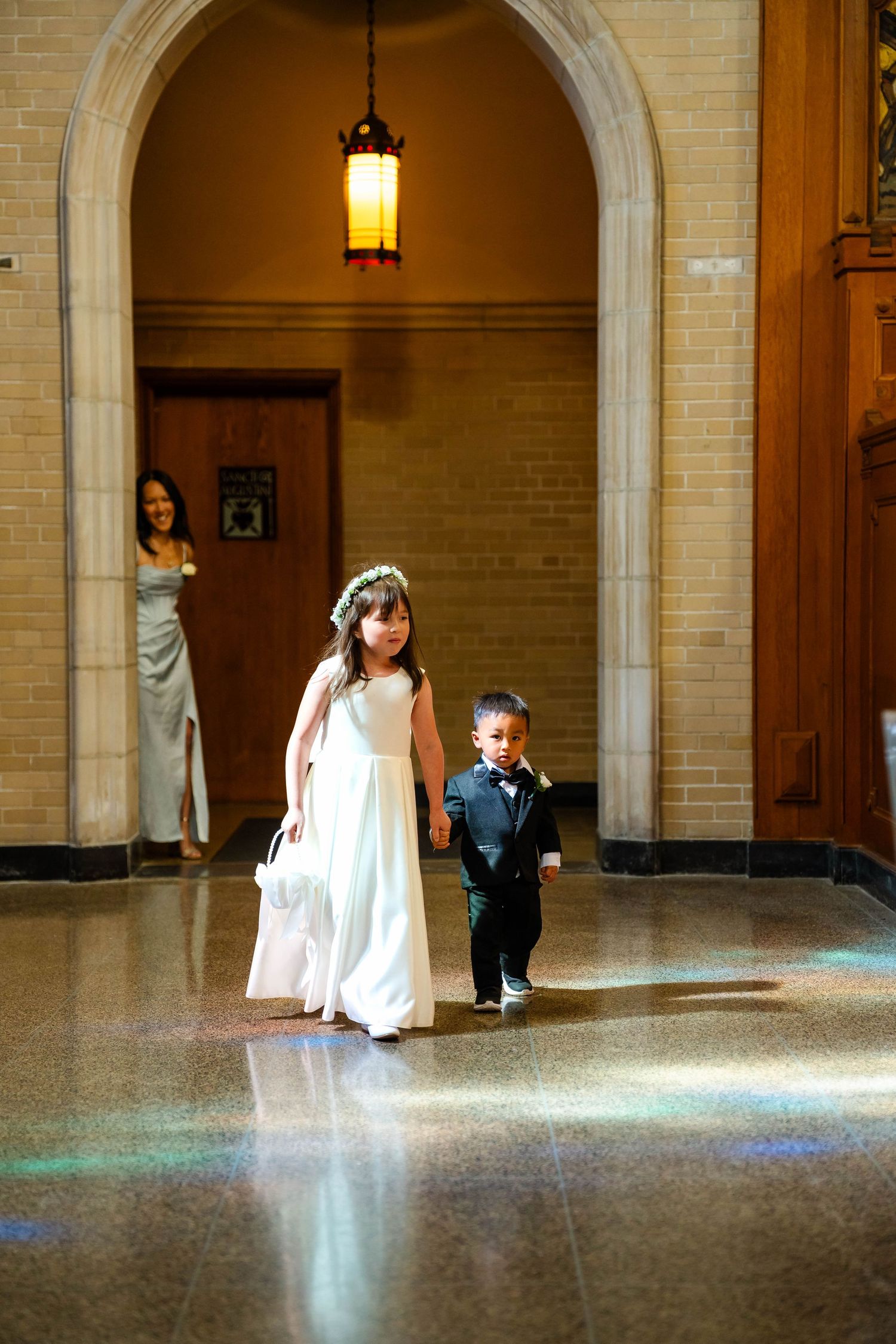 Flower girl and ring bearer walking through an arched doorway at an elegant wedding ceremony.
