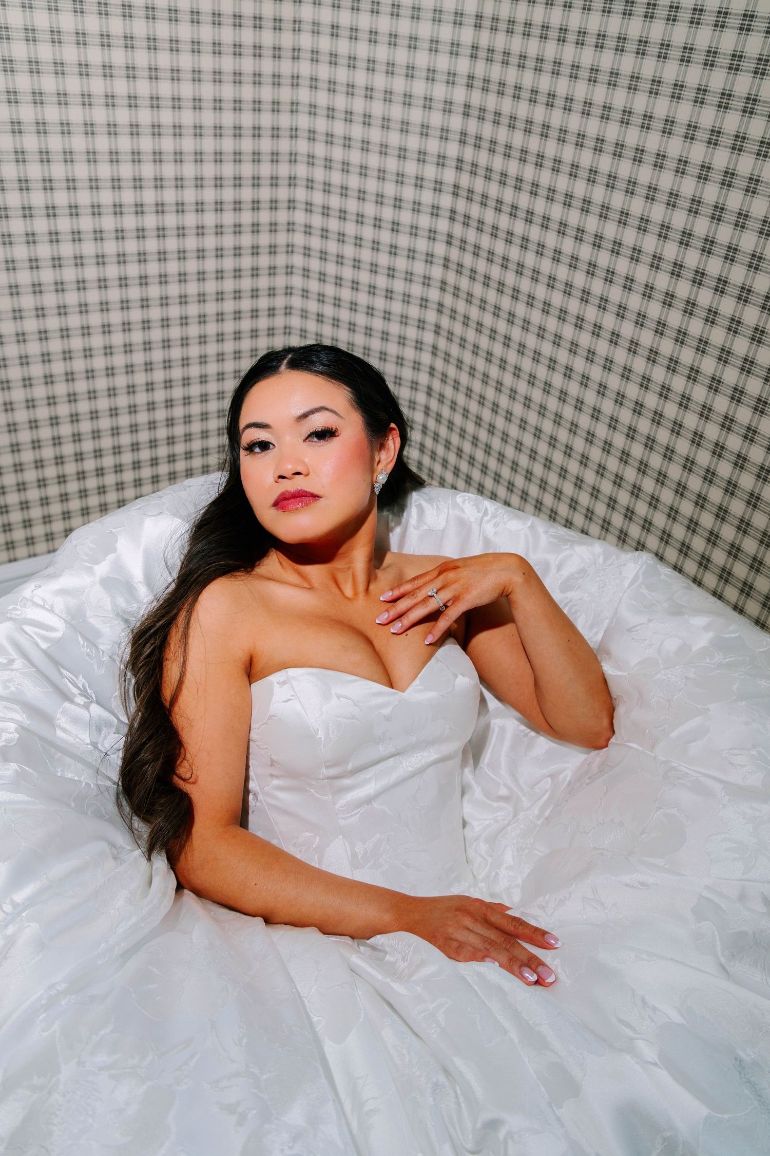 Stunning bride in a strapless white ballgown poses in a bathtub, showcasing her engagement ring and bridal look.