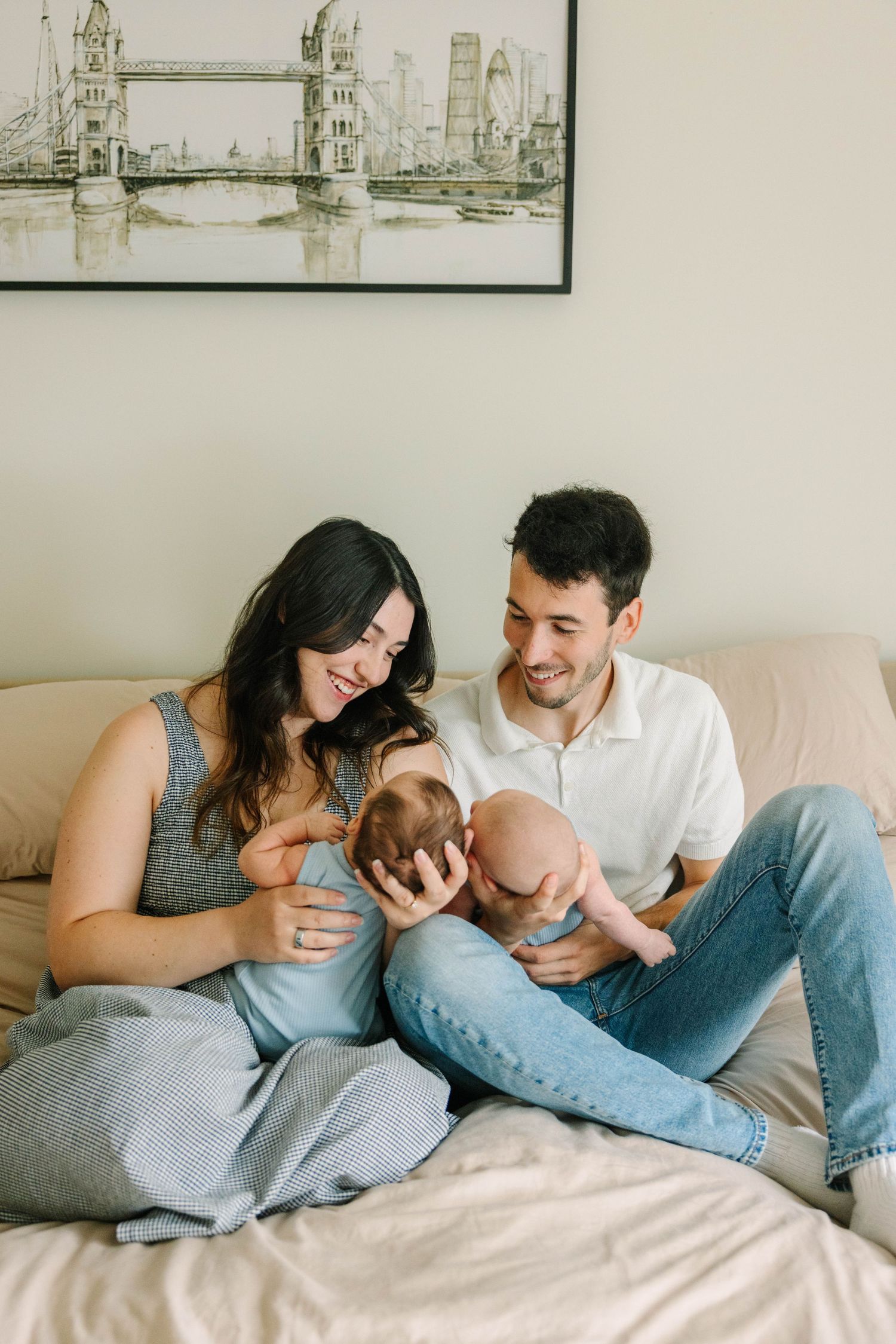 Happy young parents sitting on a bed together admiring their newborn baby.