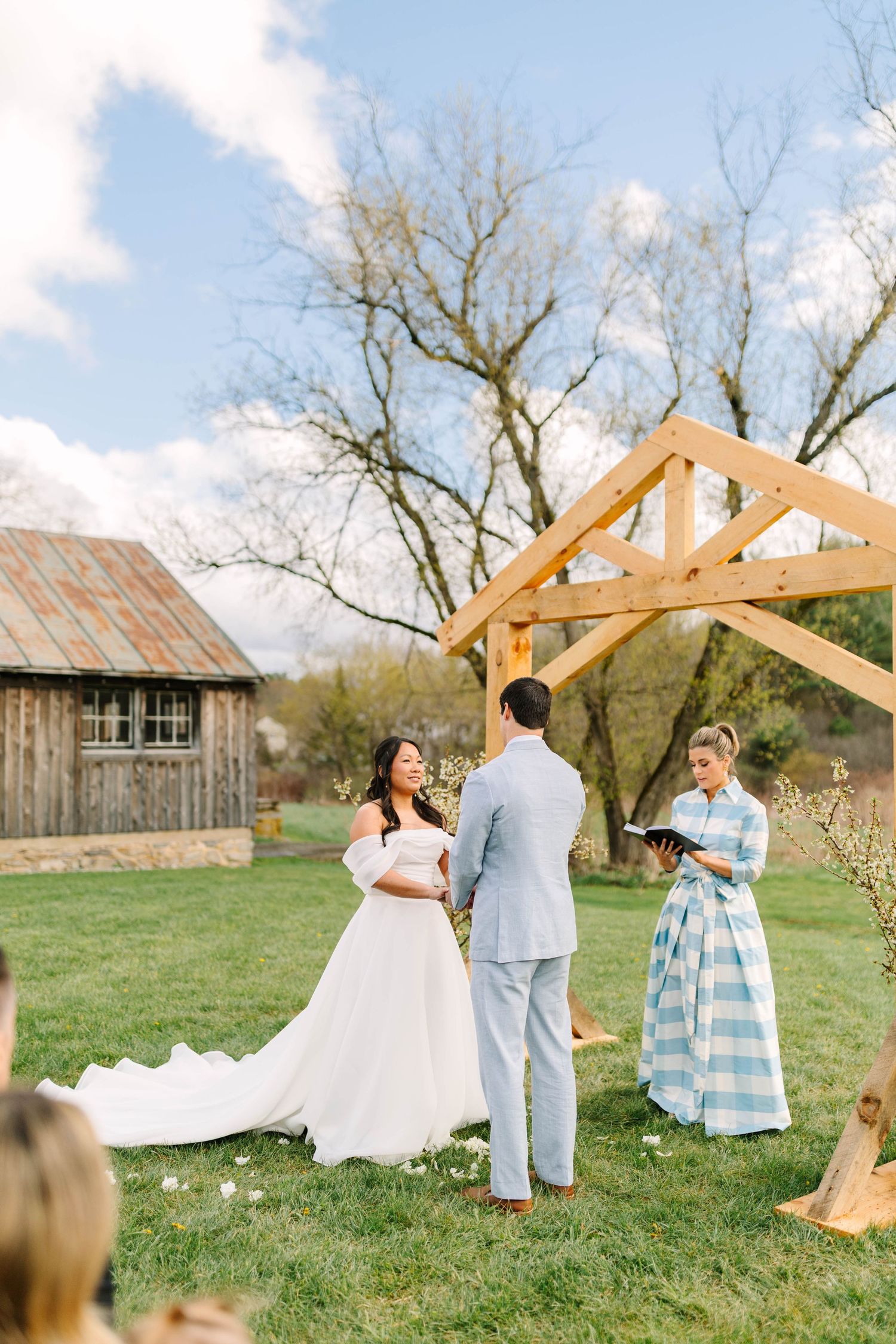Bride and groom exchange vows under a wooden arch at an outdoor farm wedding ceremony on a sunny spring day.