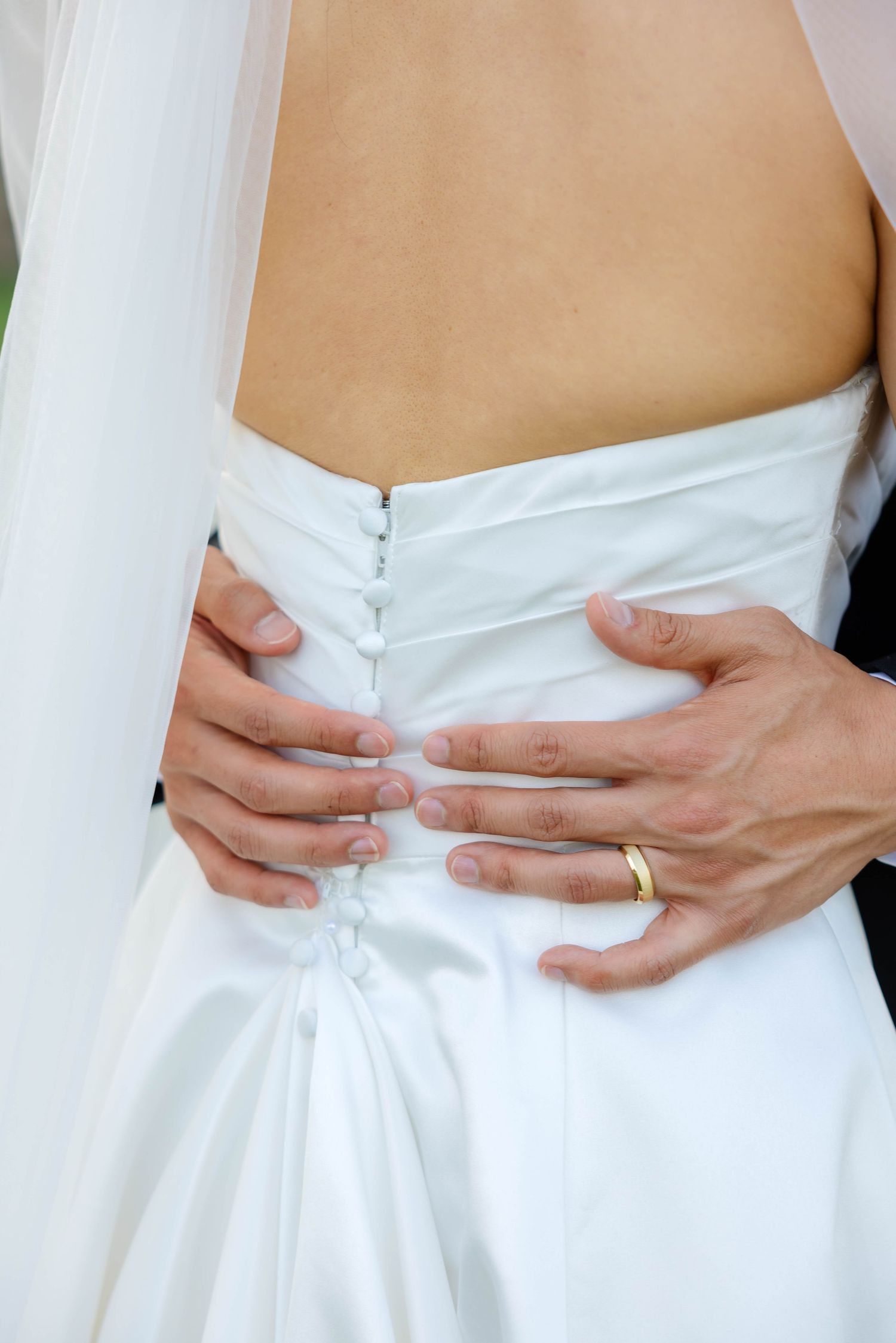 Groom placing hands on bride's waist showing wedding ring on white gown back.