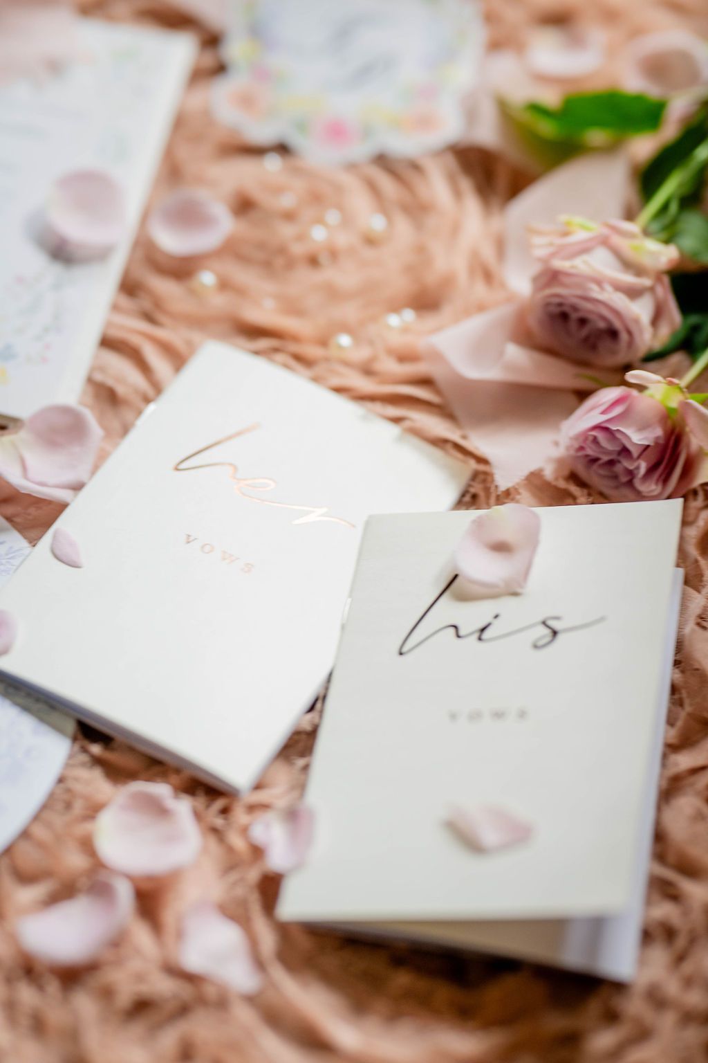 His and hers wedding vow books on blush fur with pink roses and scattered petals.