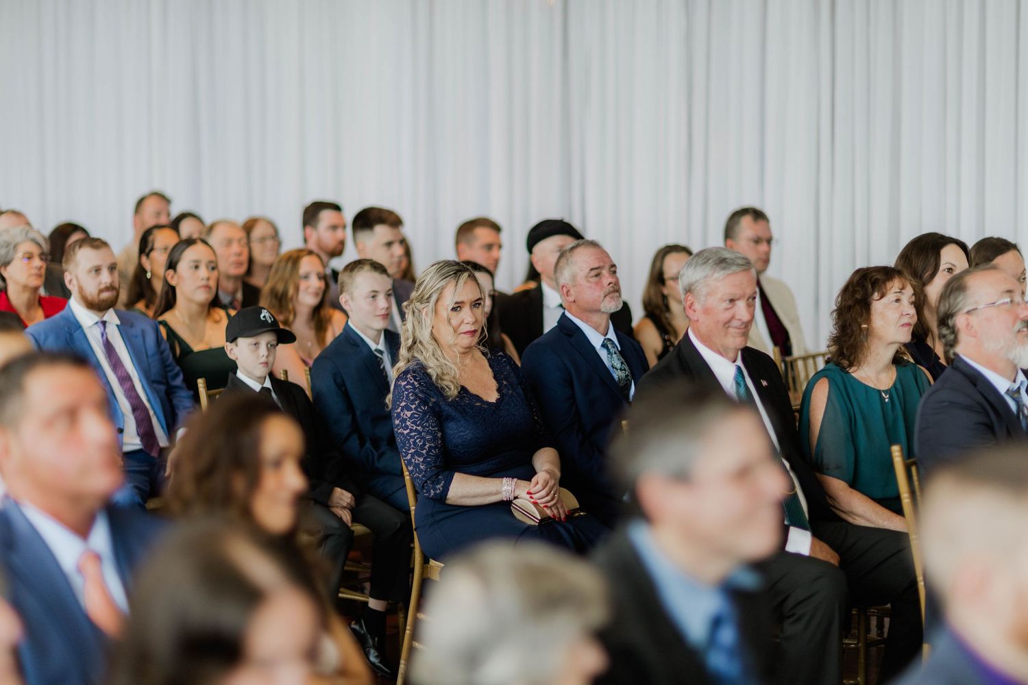 Wedding guests seated and watching ceremony attentively in elegant white draped venue.