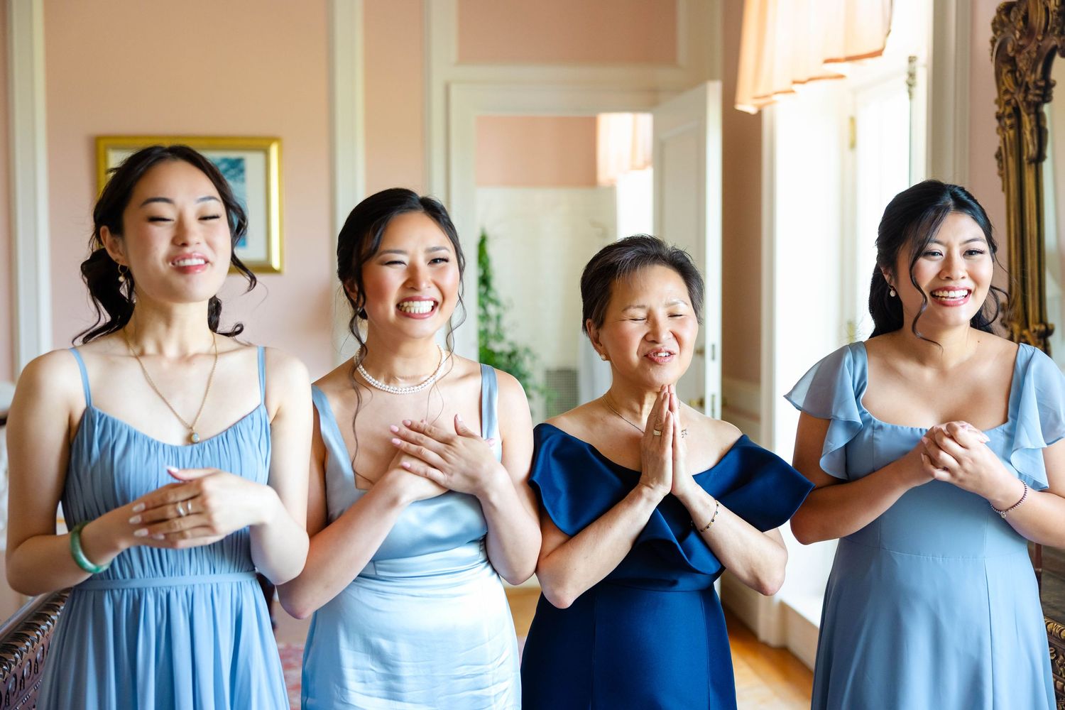 Four women in blue dresses smiling and laughing together at a wedding celebration indoors.