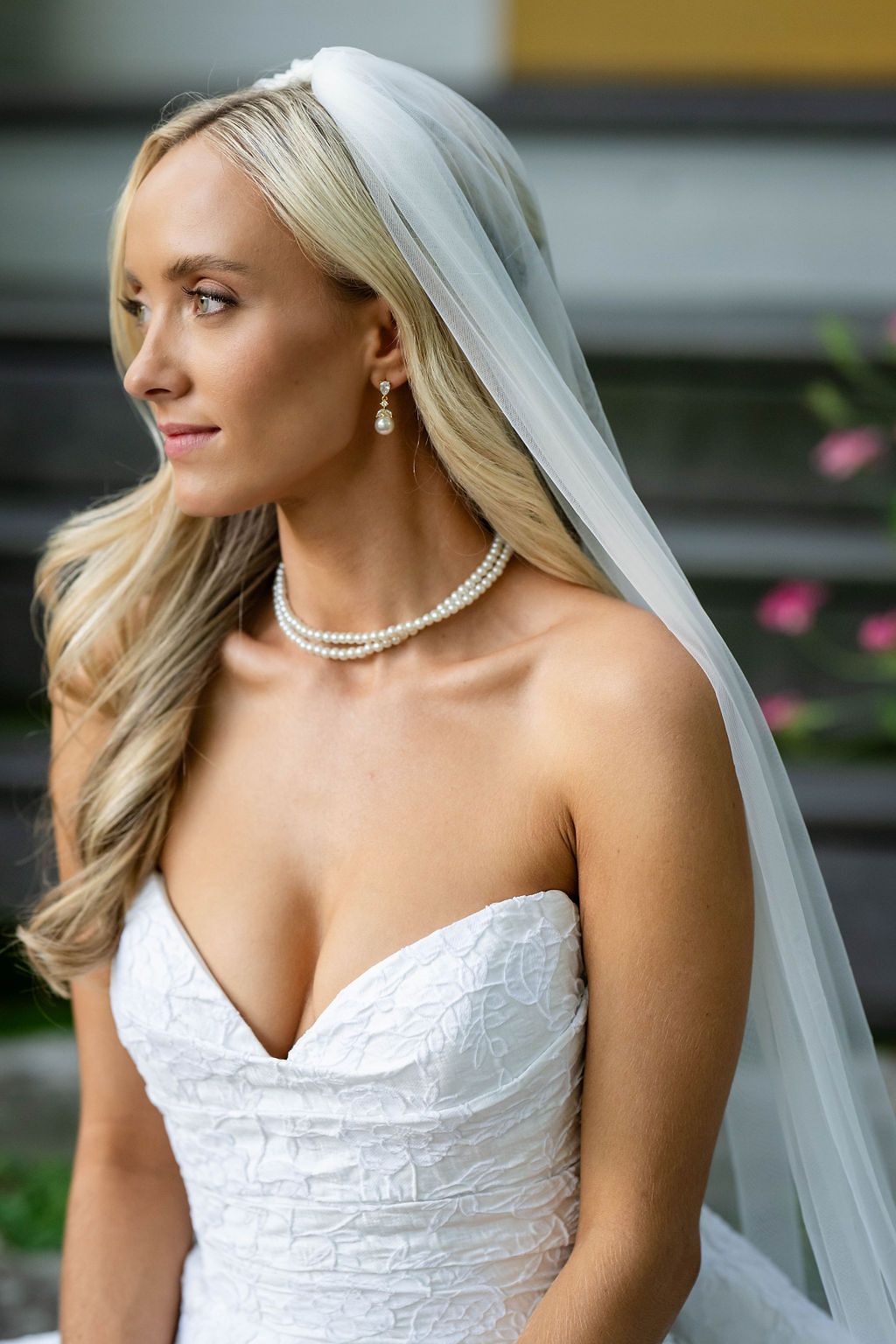 Beautiful blonde bride wearing pearl necklace and earrings with a white veil and strapless lace gown.