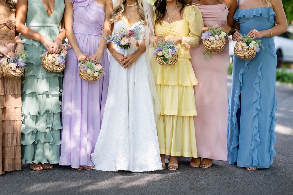 Bride in white gown with bridesmaids in pastel multicolor dresses holding floral bouquets at a wedding.