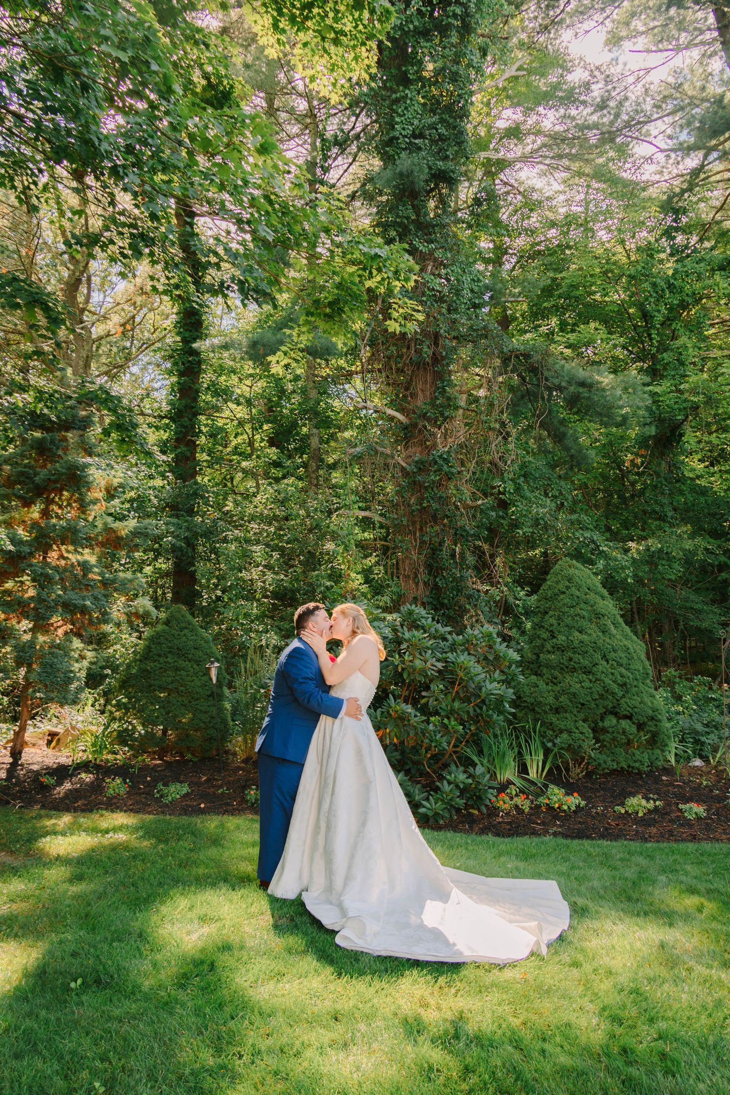 Bride and groom share a romantic kiss in a lush green garden on their wedding day.