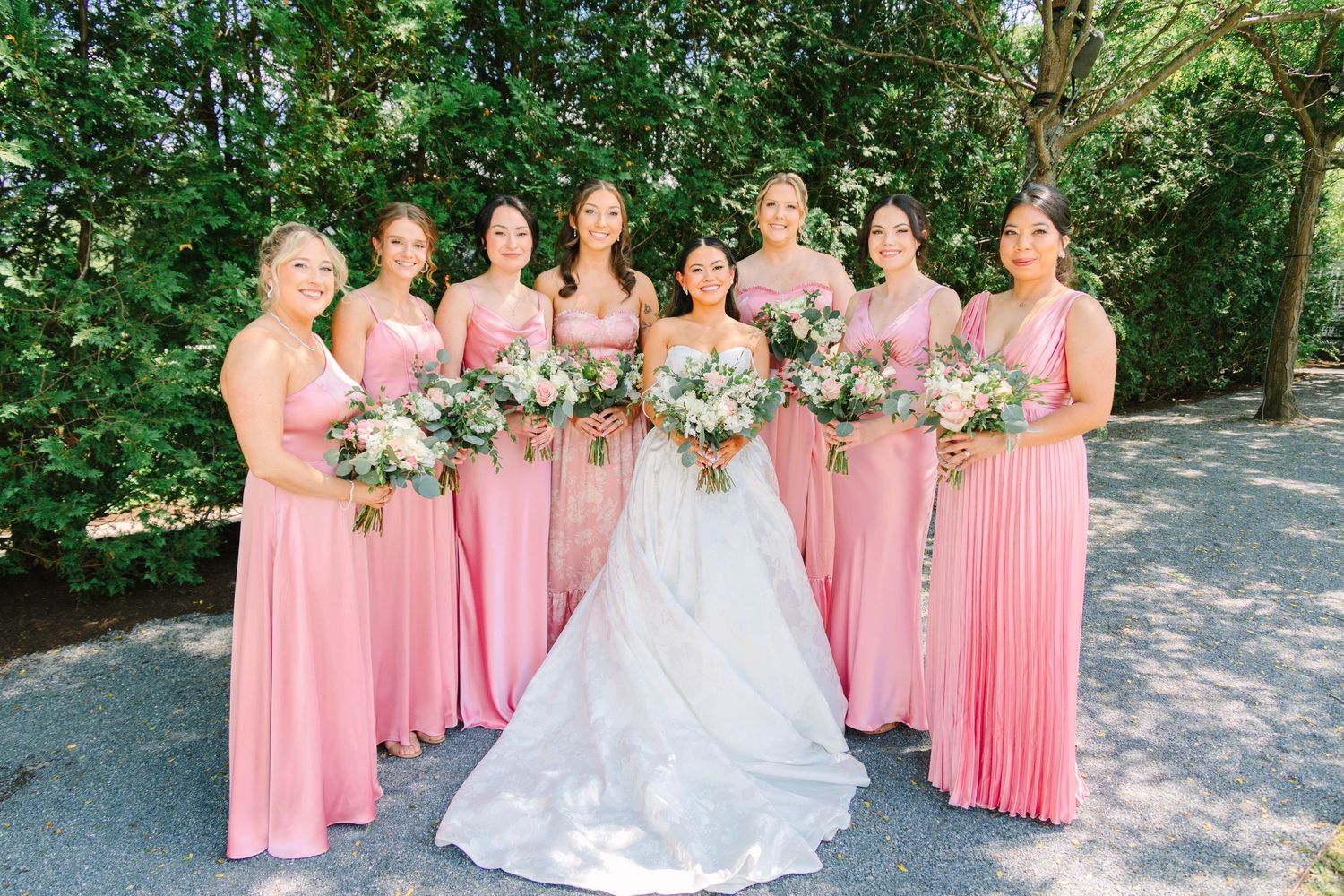 Bride in white ballgown poses with six bridesmaids in pink dresses holding floral bouquets.