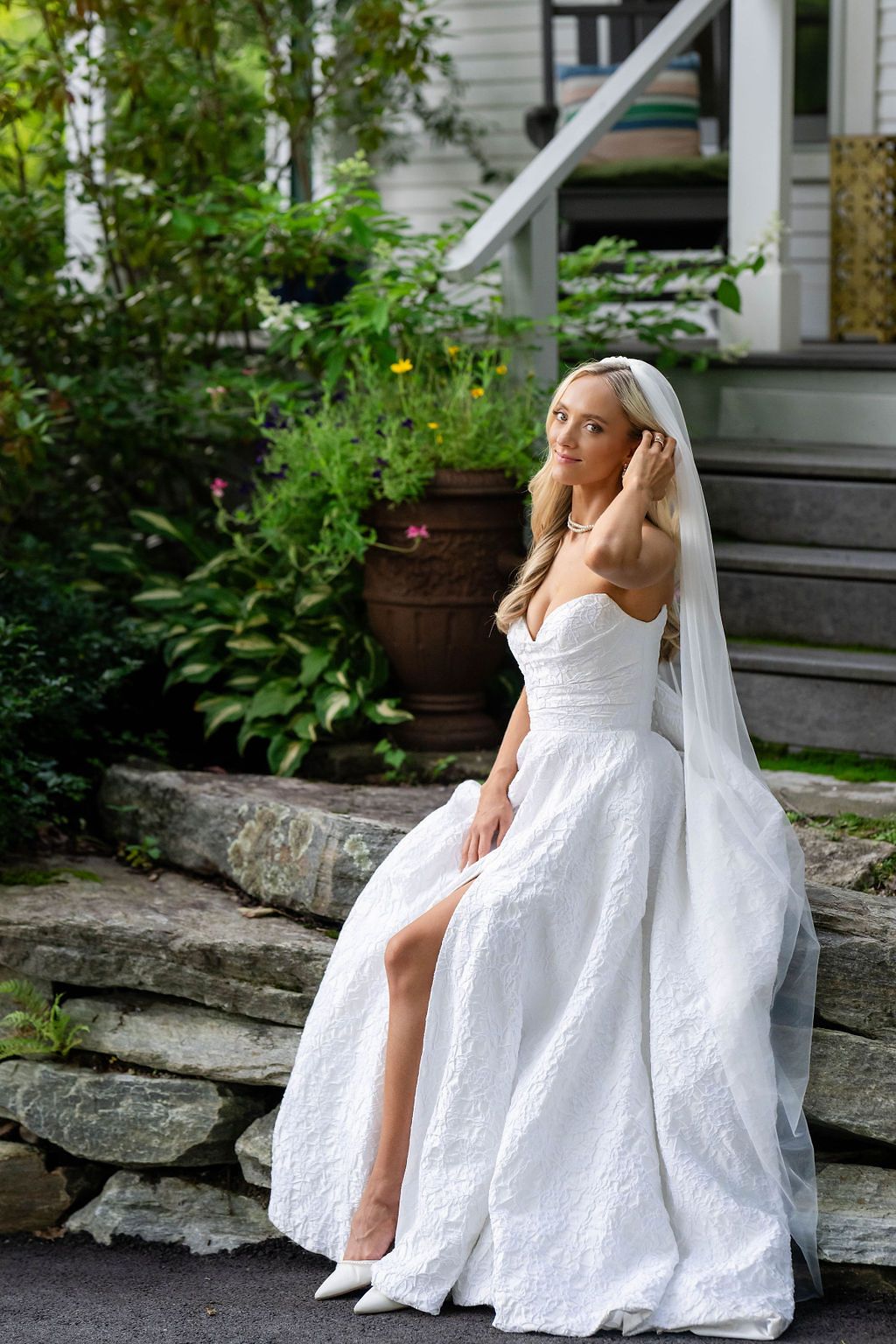 Beautiful blonde bride in white lace wedding dress with veil poses on stone steps.