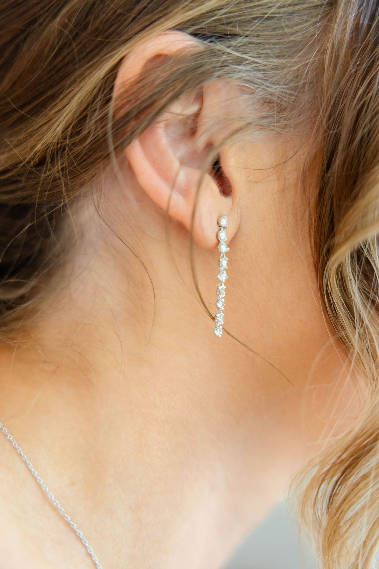 Close-up detail of bride's elegant dangling diamond drop earring with delicate chain necklace.