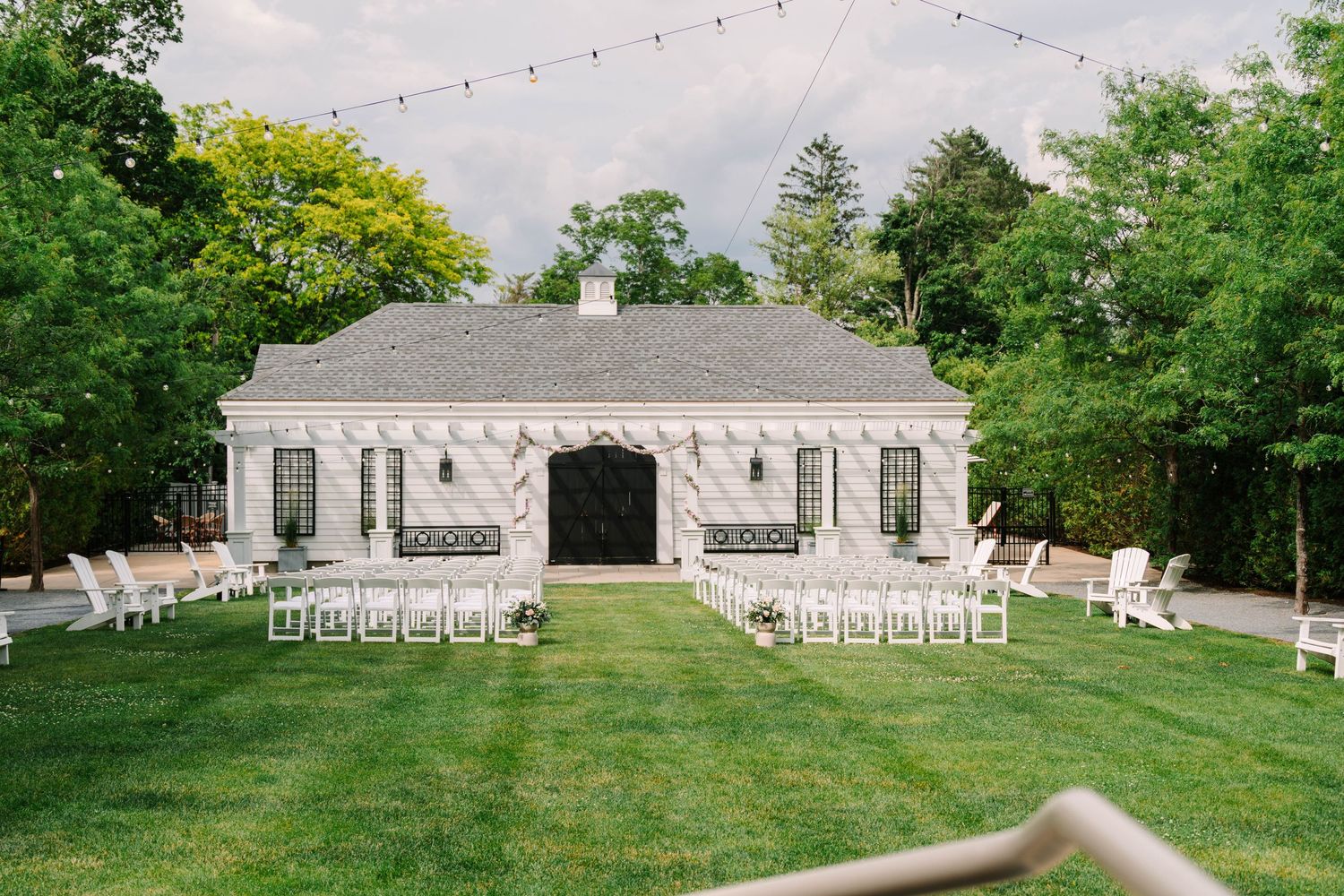 Aerial view of white barn wedding venue with rows of white chairs arranged on manicured green lawn.