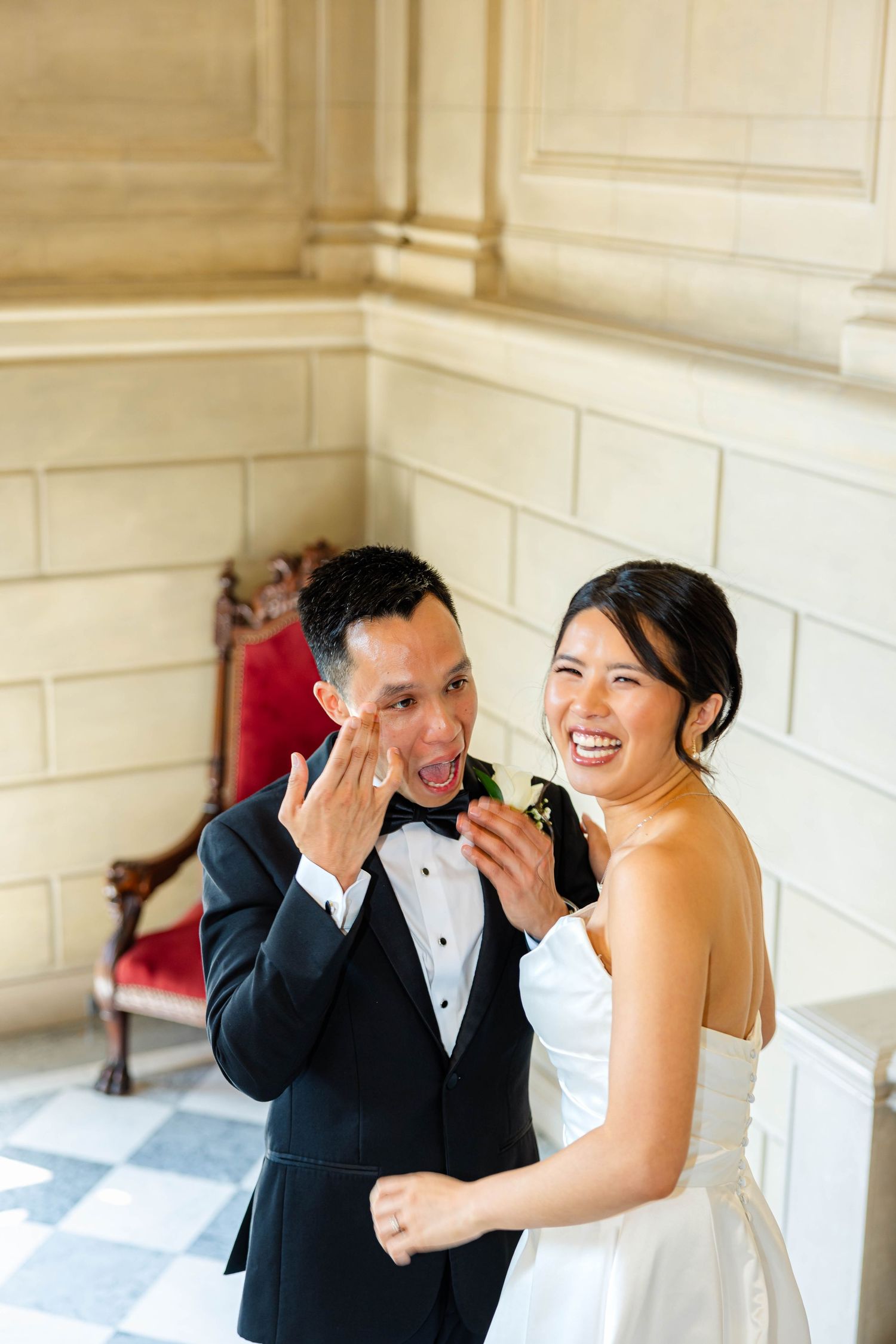 Asian bride and groom laughing joyfully while showing off wedding rings in an elegant venue.