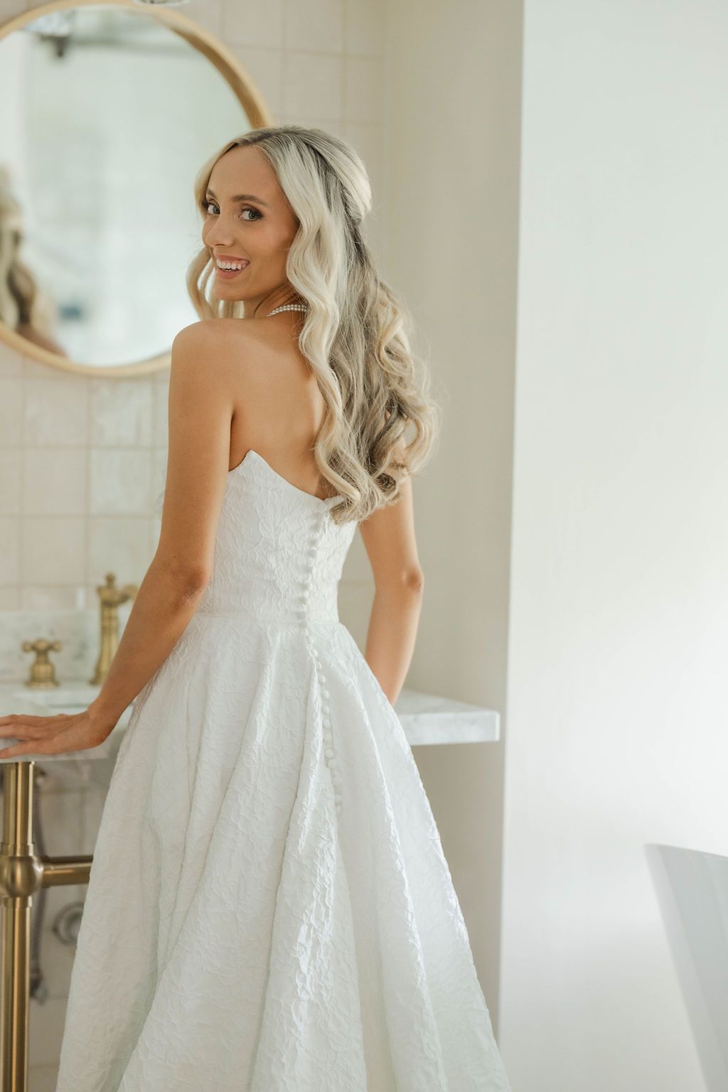Smiling bride in strapless lace ball gown with elegant curled blonde hair.