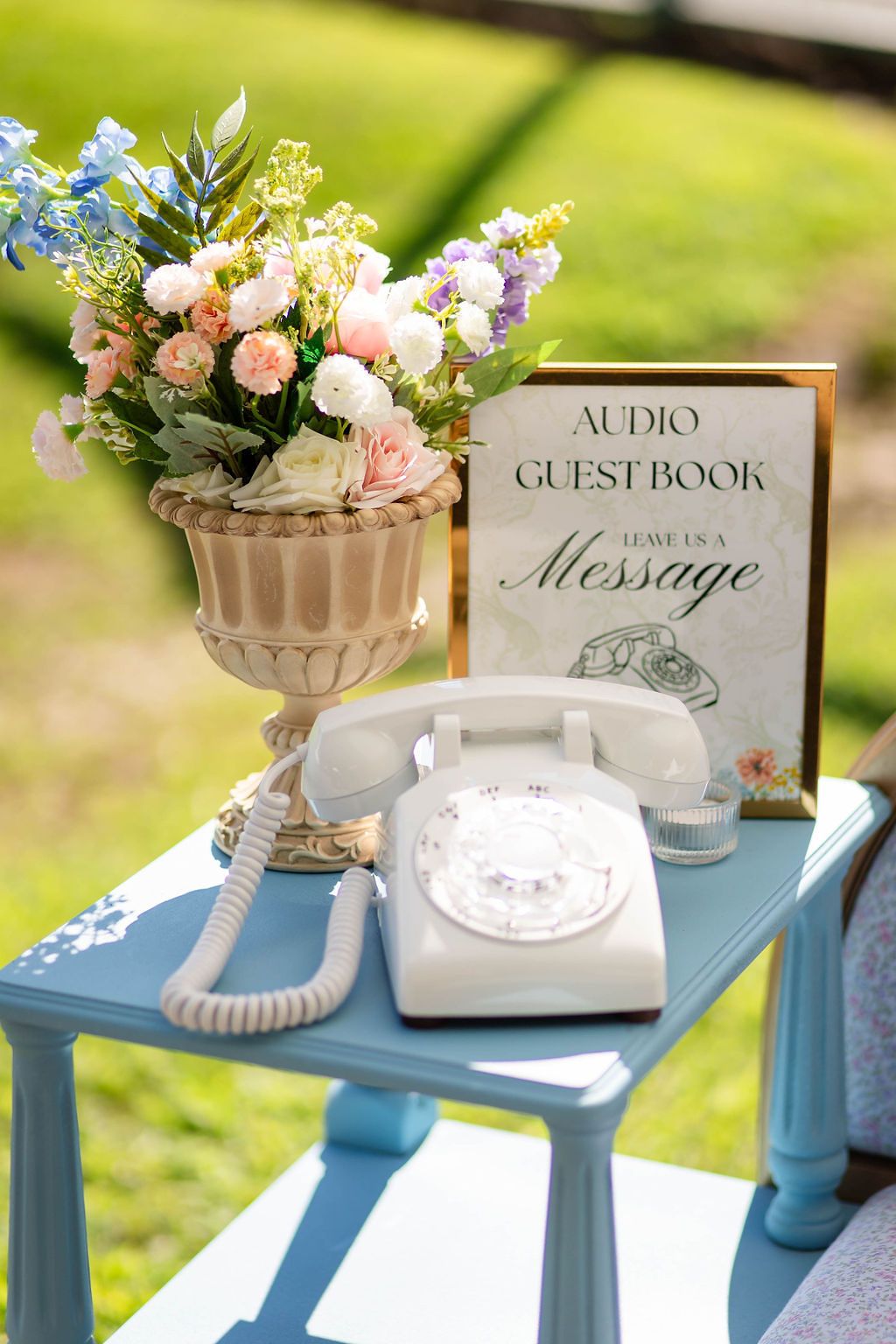 Vintage white rotary phone audio guestbook display with floral arrangement at an outdoor wedding.