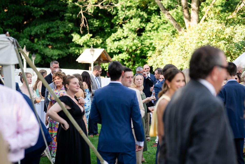 Wedding guests mingle outdoors under trees during garden reception cocktail hour.