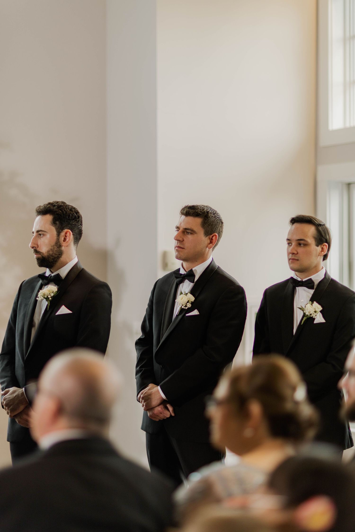 Three groomsmen in black tuxedos with boutonnieres standing at wedding ceremony altar.