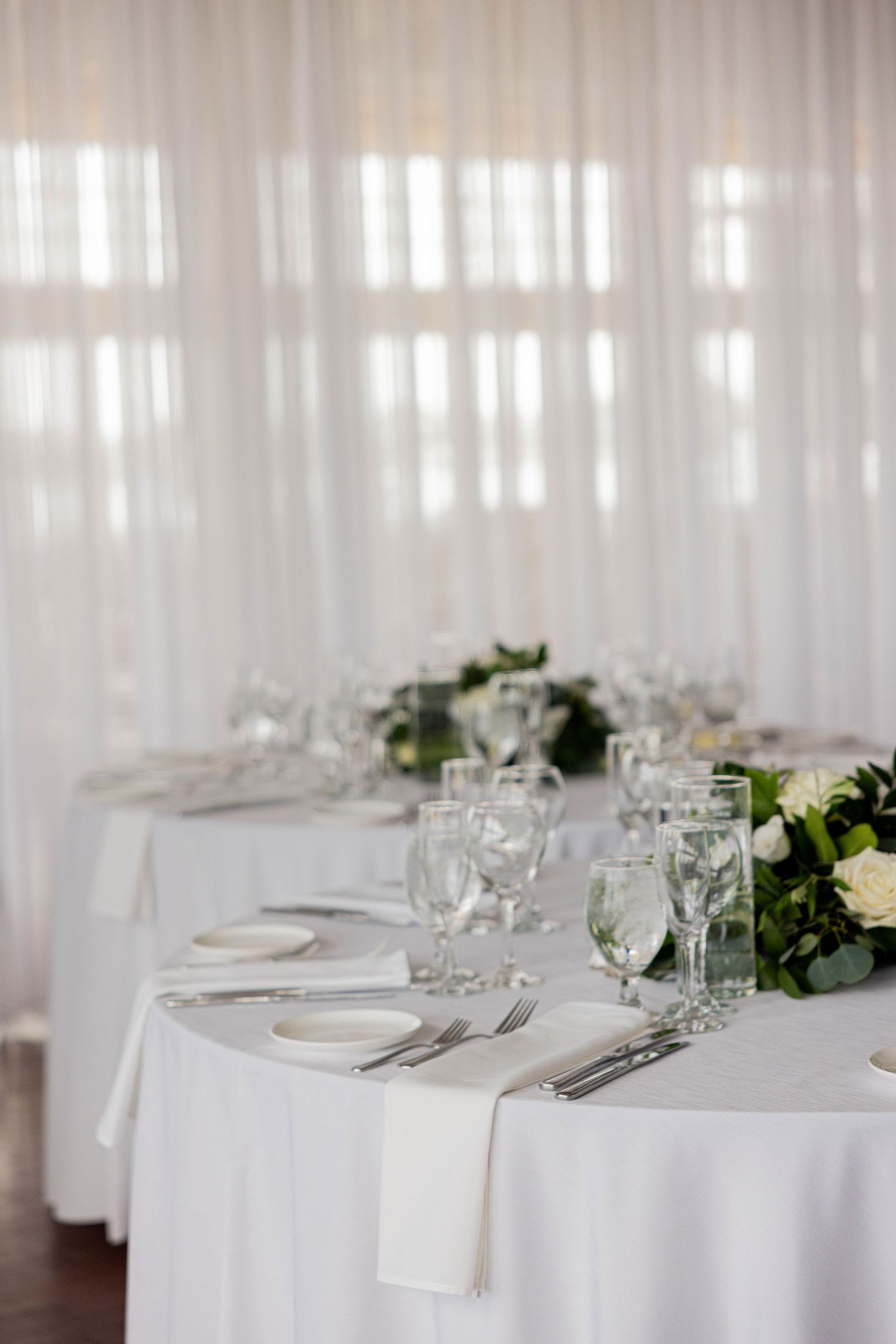 Elegant wedding reception tables with white linens, crystal glasses, and white floral centerpieces.