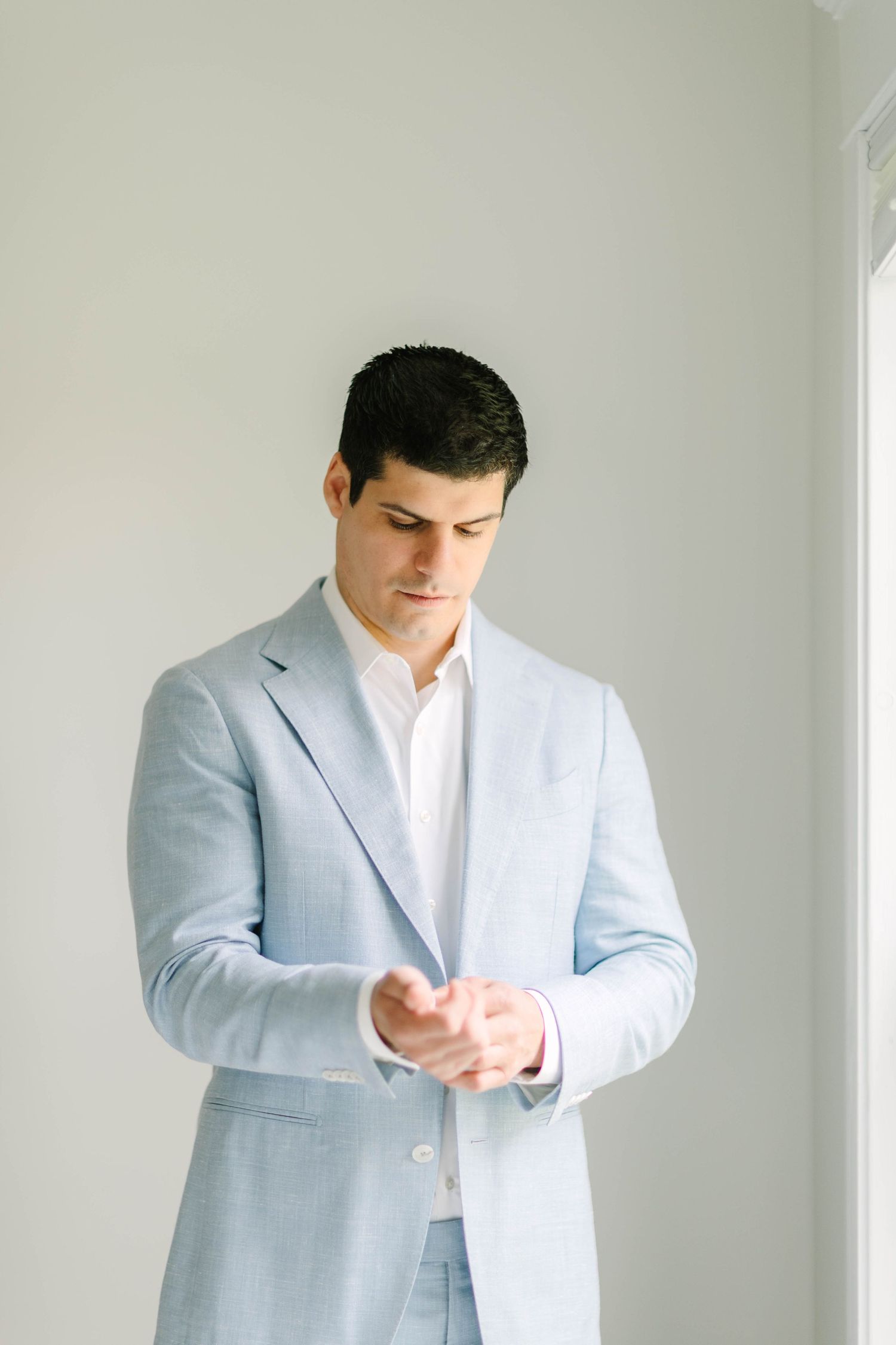 Groom in light blue suit adjusting his cuff links while getting ready for his wedding.