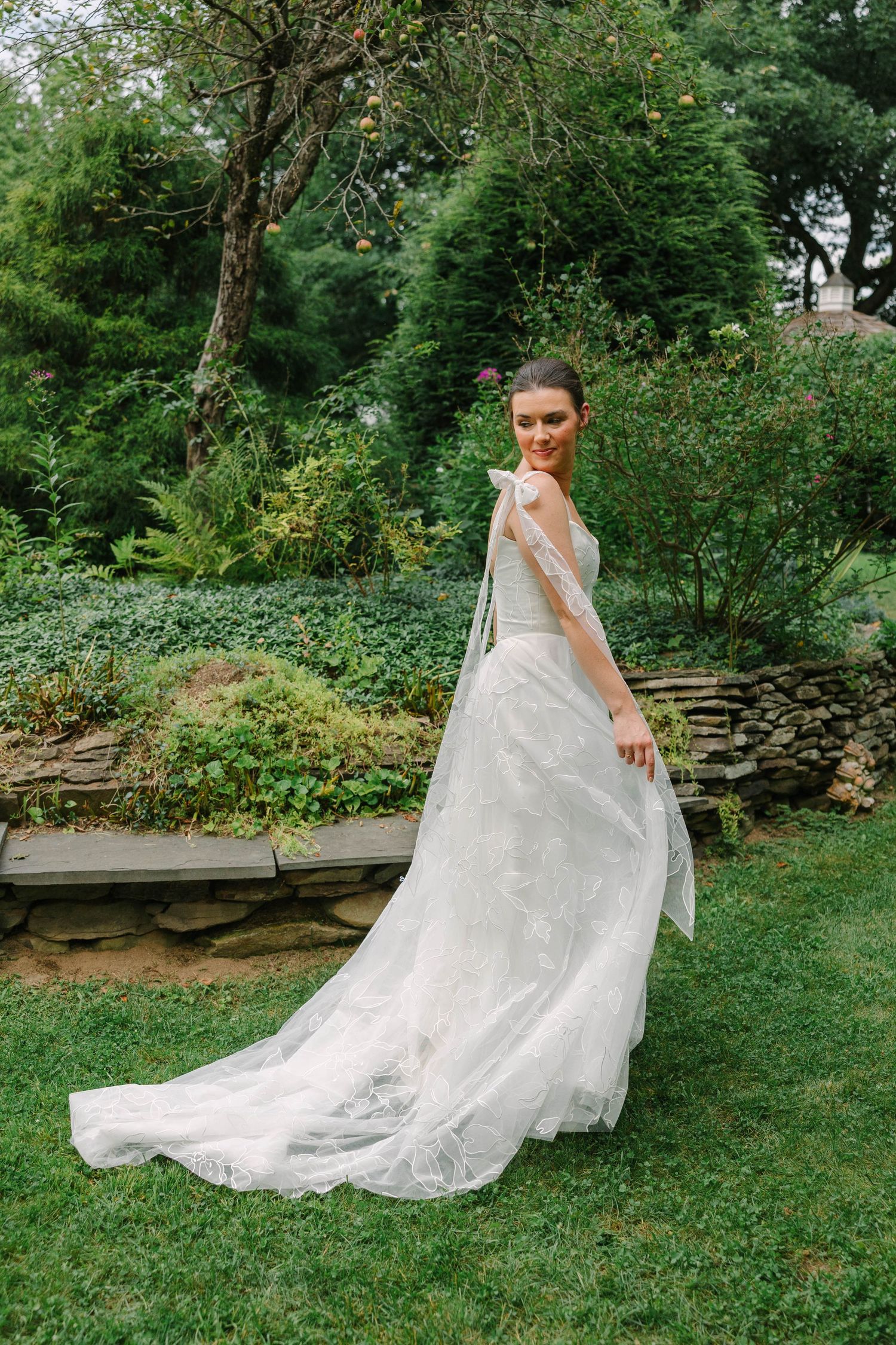 Bride twirling in elegant white lace wedding gown with flowing train in lush garden setting.