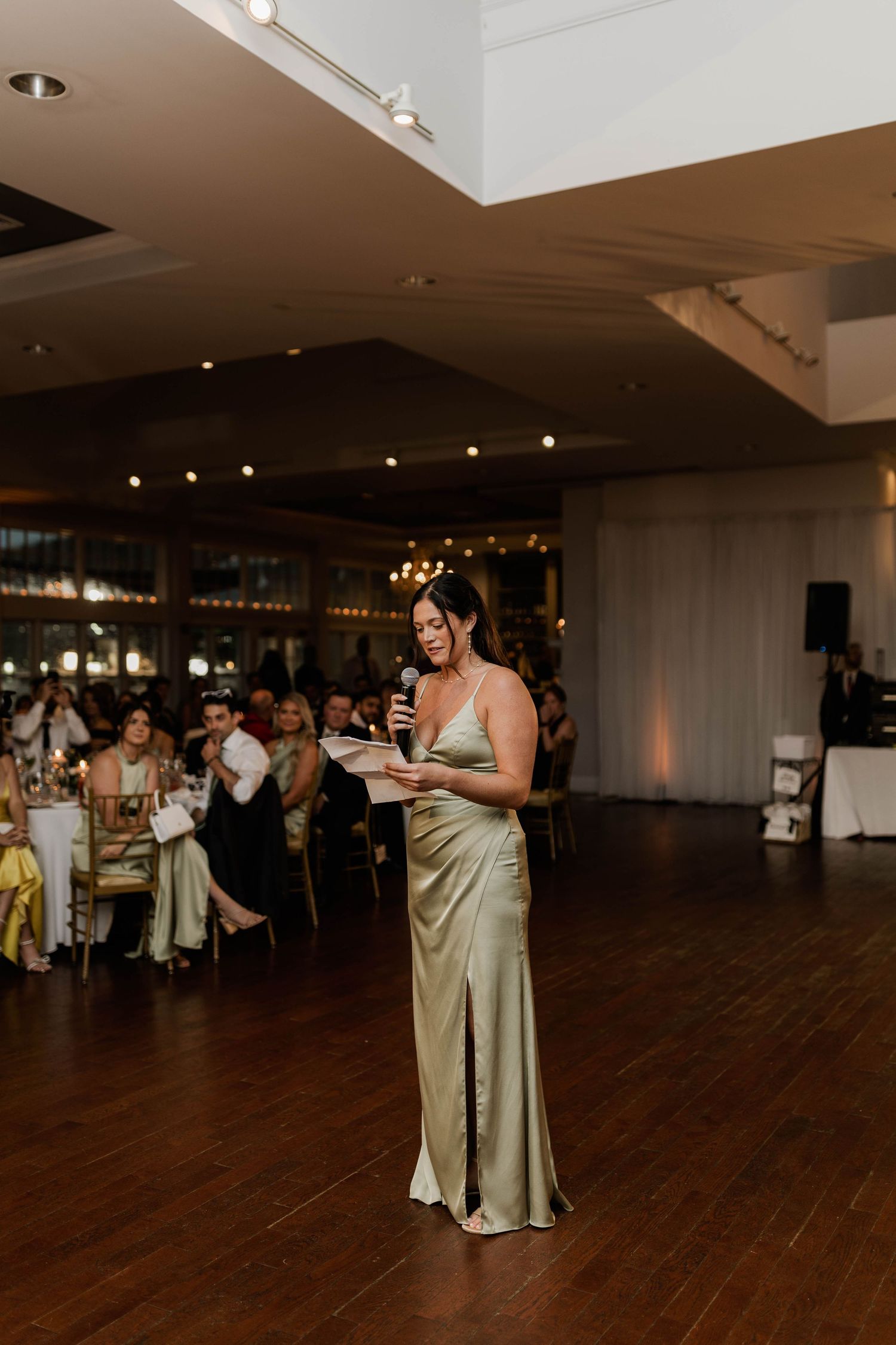 Bridesmaid in gold satin gown delivers heartfelt speech at wedding reception.
