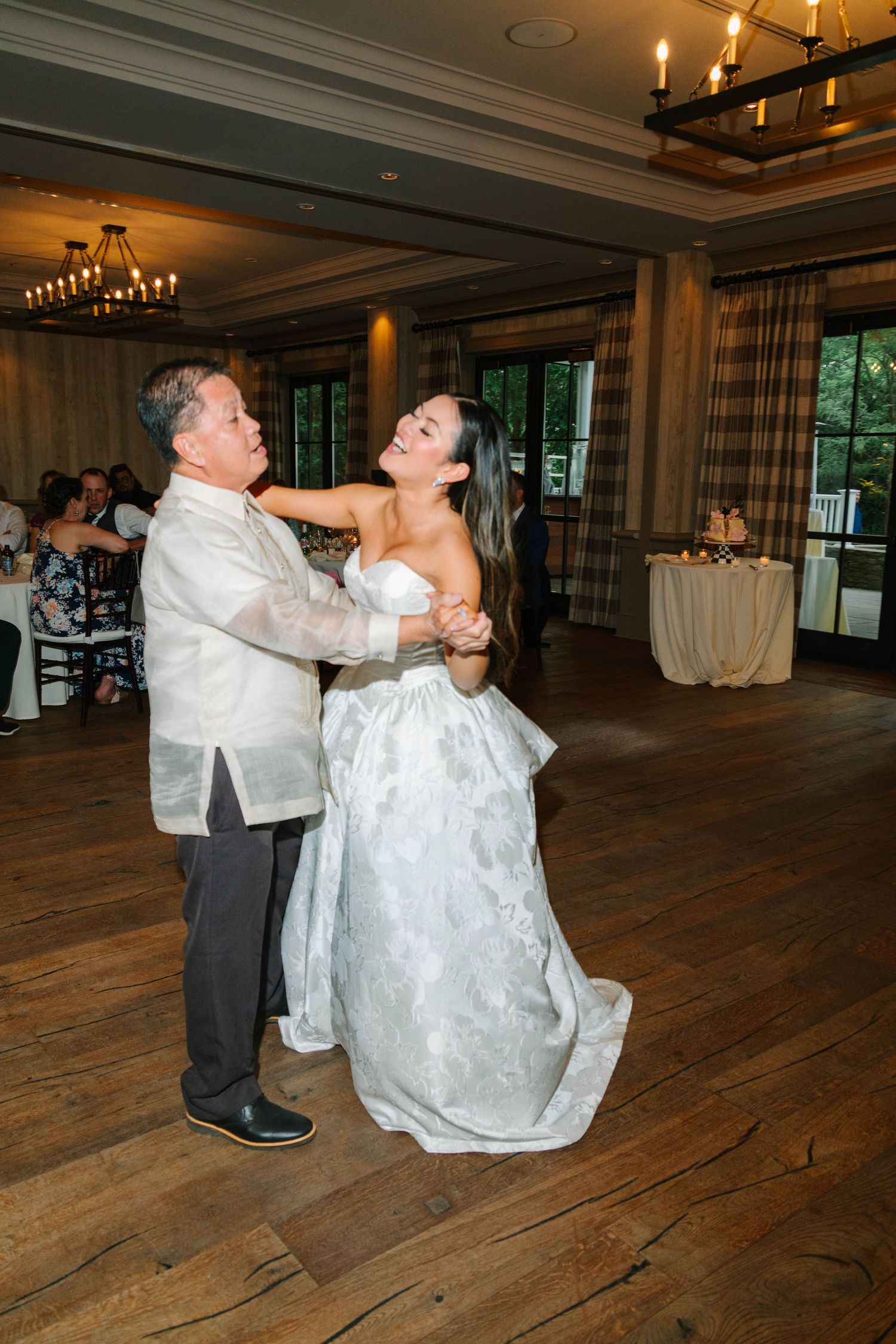 Bride laughs joyfully while dancing with her father at elegant wedding reception.