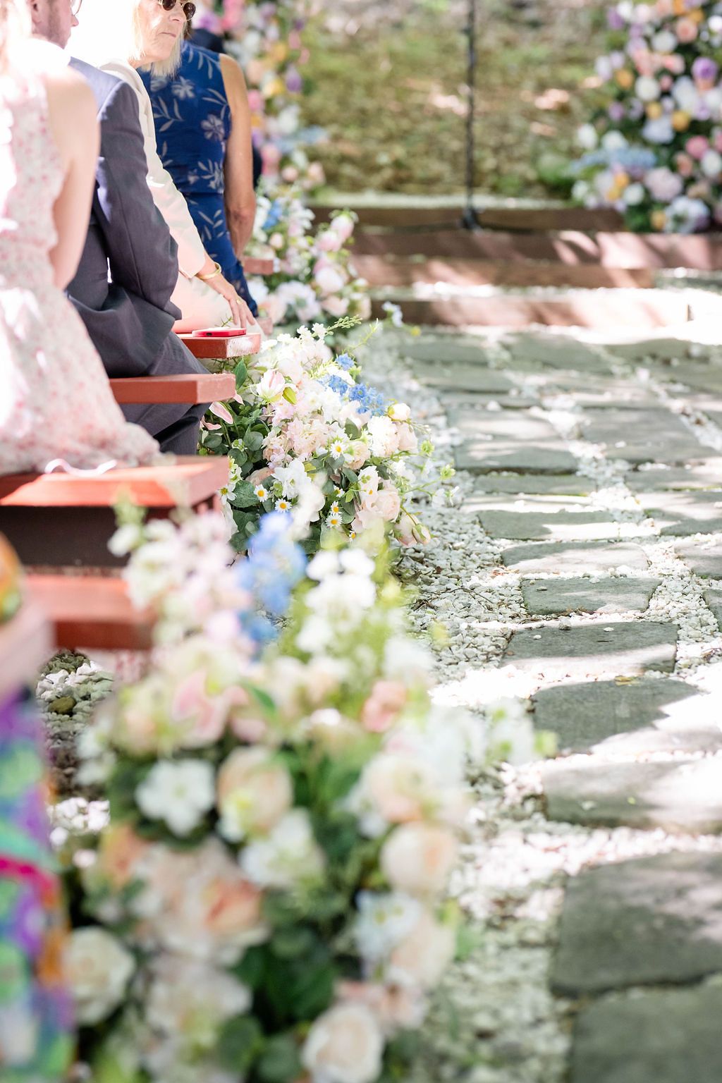 Elegant outdoor wedding ceremony aisle lined with pastel floral arrangements on stone pathway.