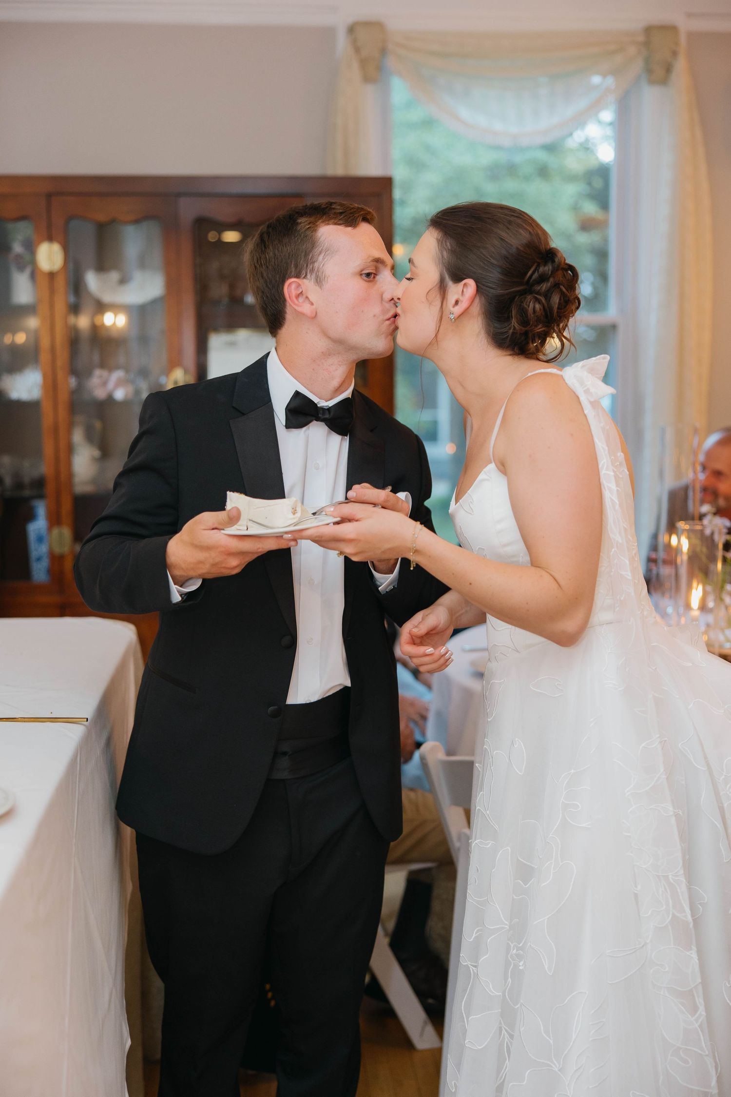 Bride and groom sharing a kiss while cutting wedding cake at elegant indoor reception.