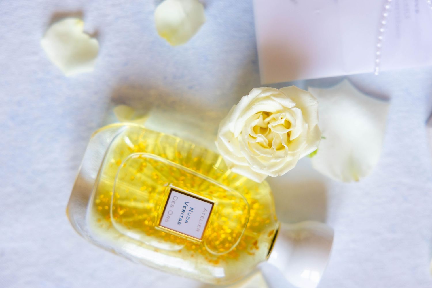 Elegant yellow perfume bottle surrounded by white rose petals and ribbon on a soft white background.