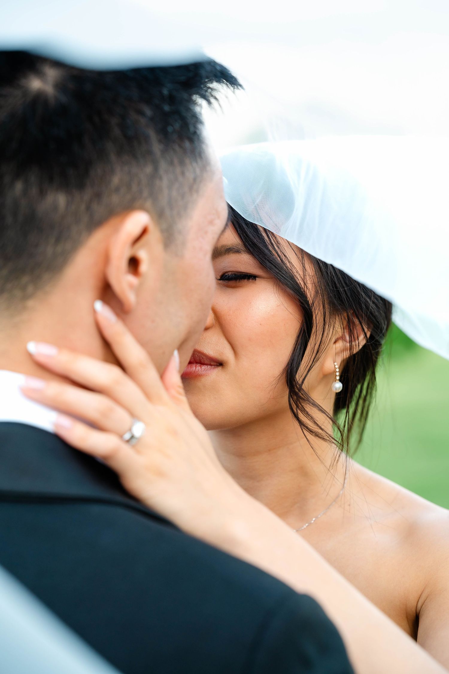Bride with wedding veil tenderly touches grooms face showing diamond ring.