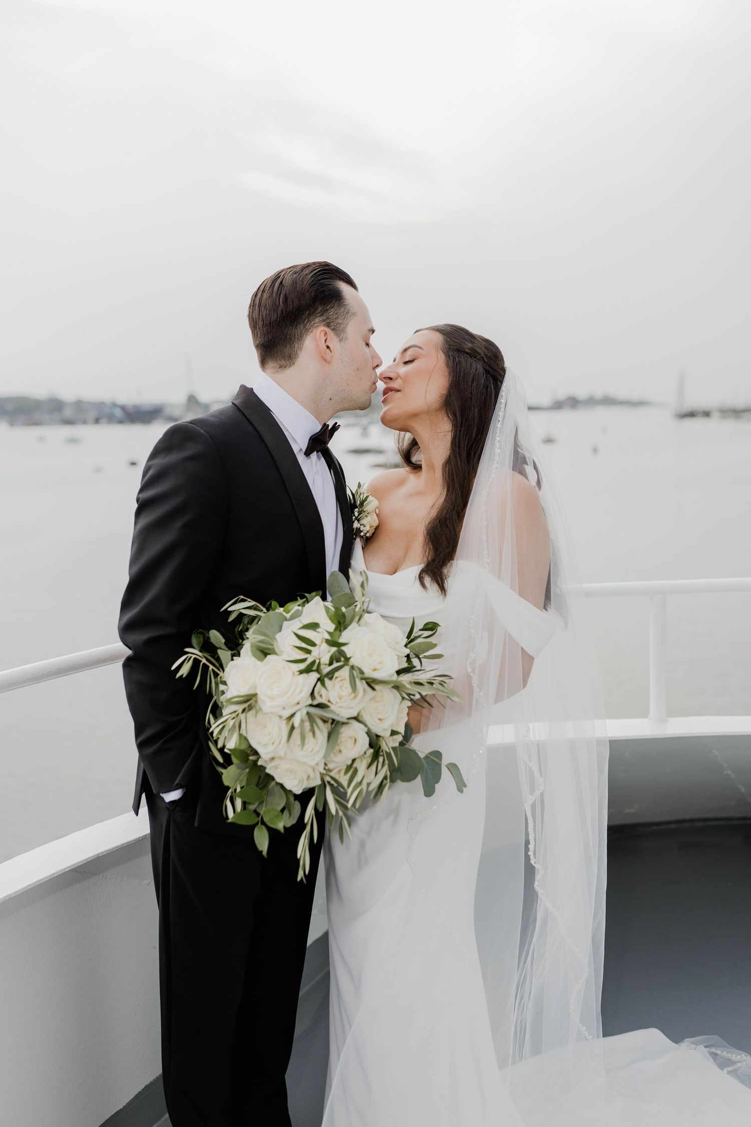 Bride and groom sharing intimate moment on yacht deck with white rose bouquet.