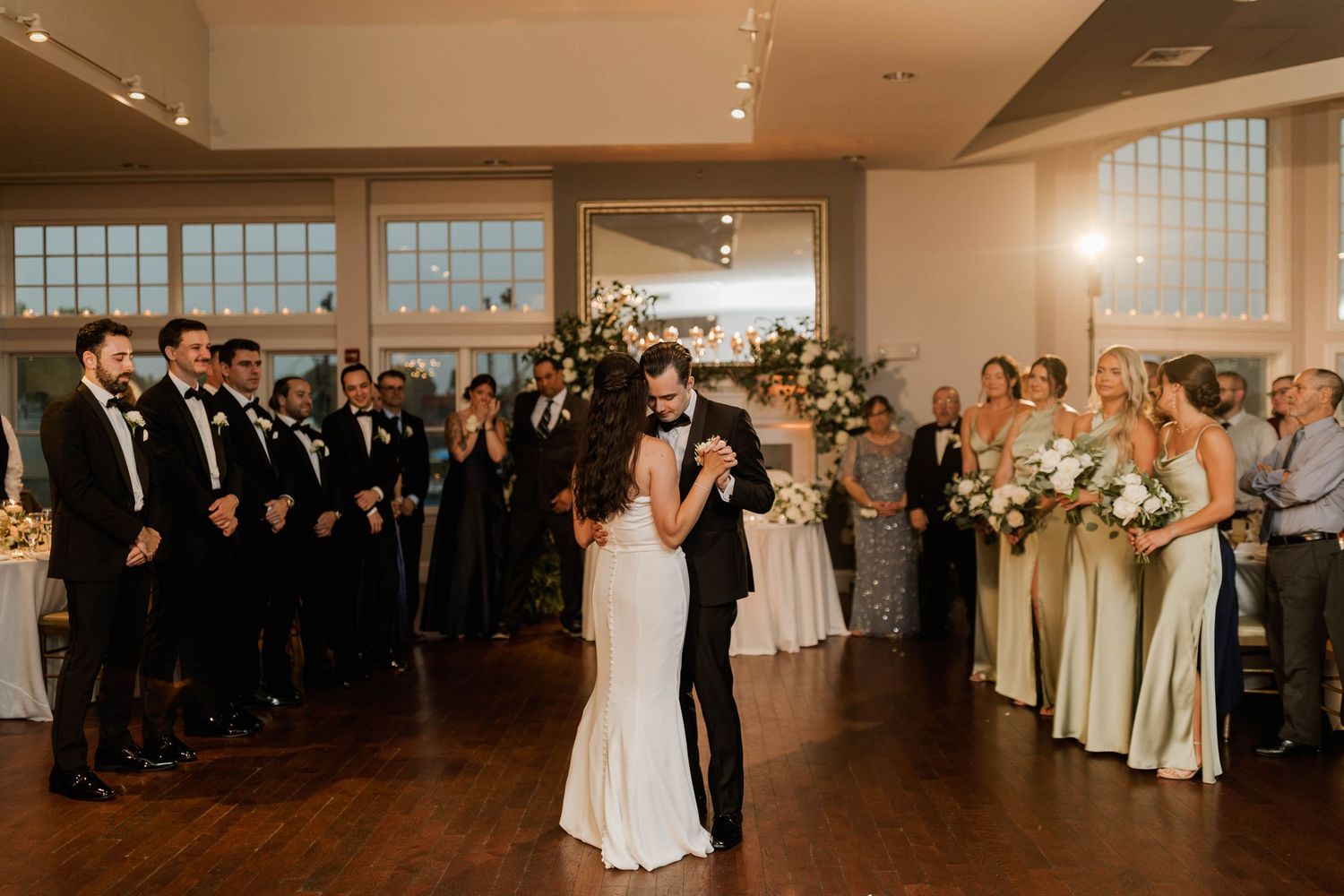 Bride and groom sharing their first dance surrounded by wedding party in an elegant reception venue.
