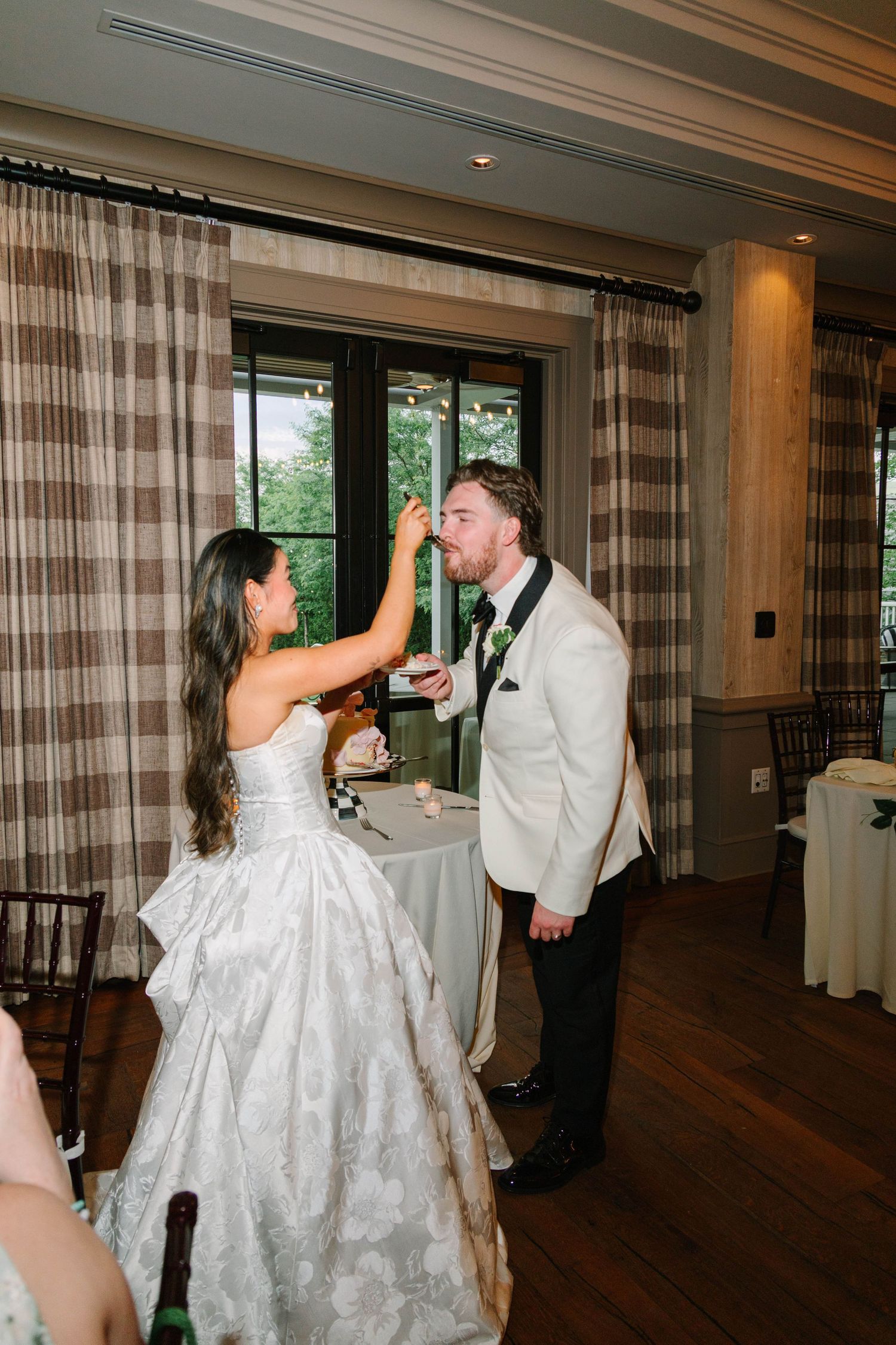 Bride playfully feeds groom wedding cake during joyful reception celebration indoors.