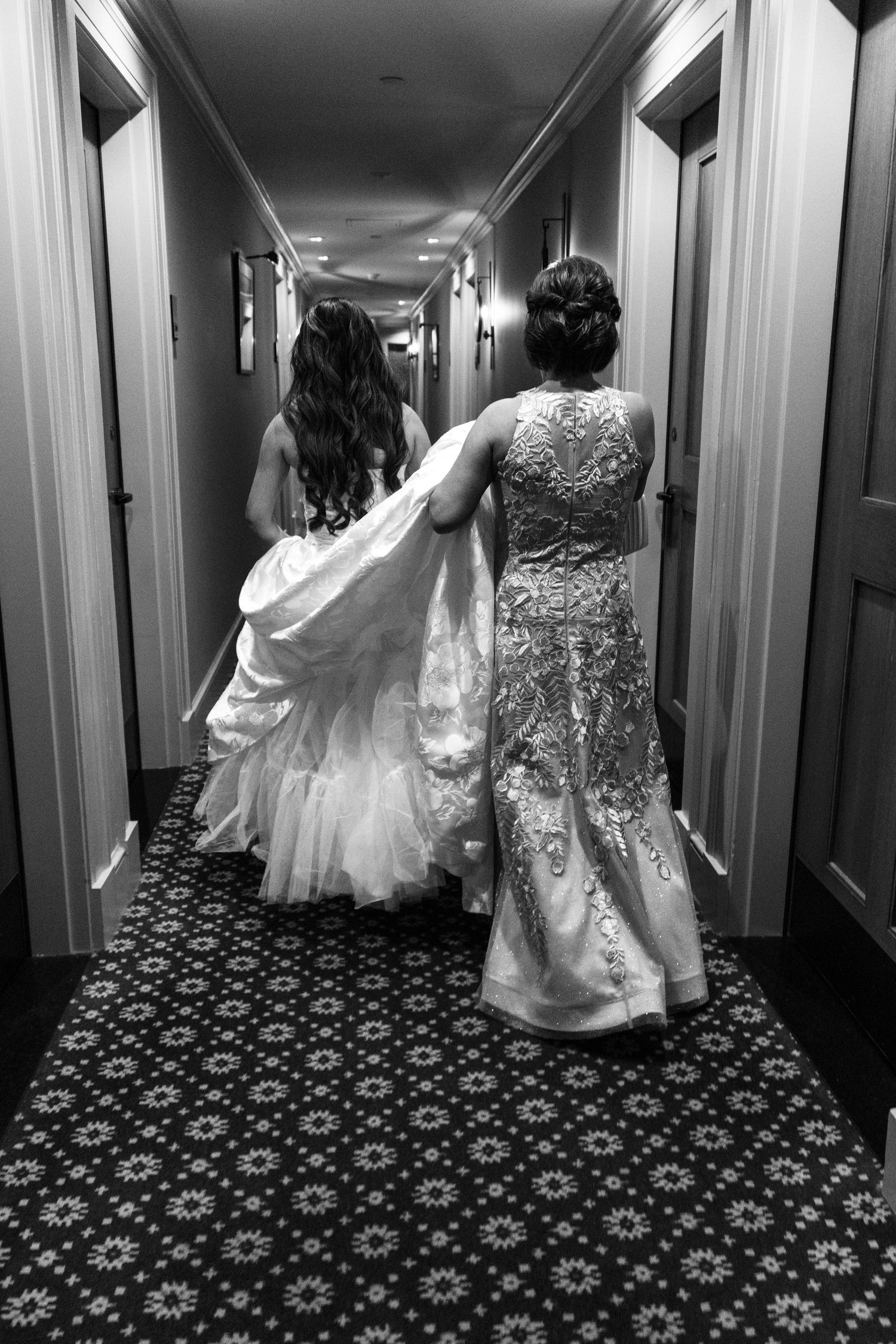 Black and white photo of a bride and her mother walking down a hotel hallway before the wedding ceremony.