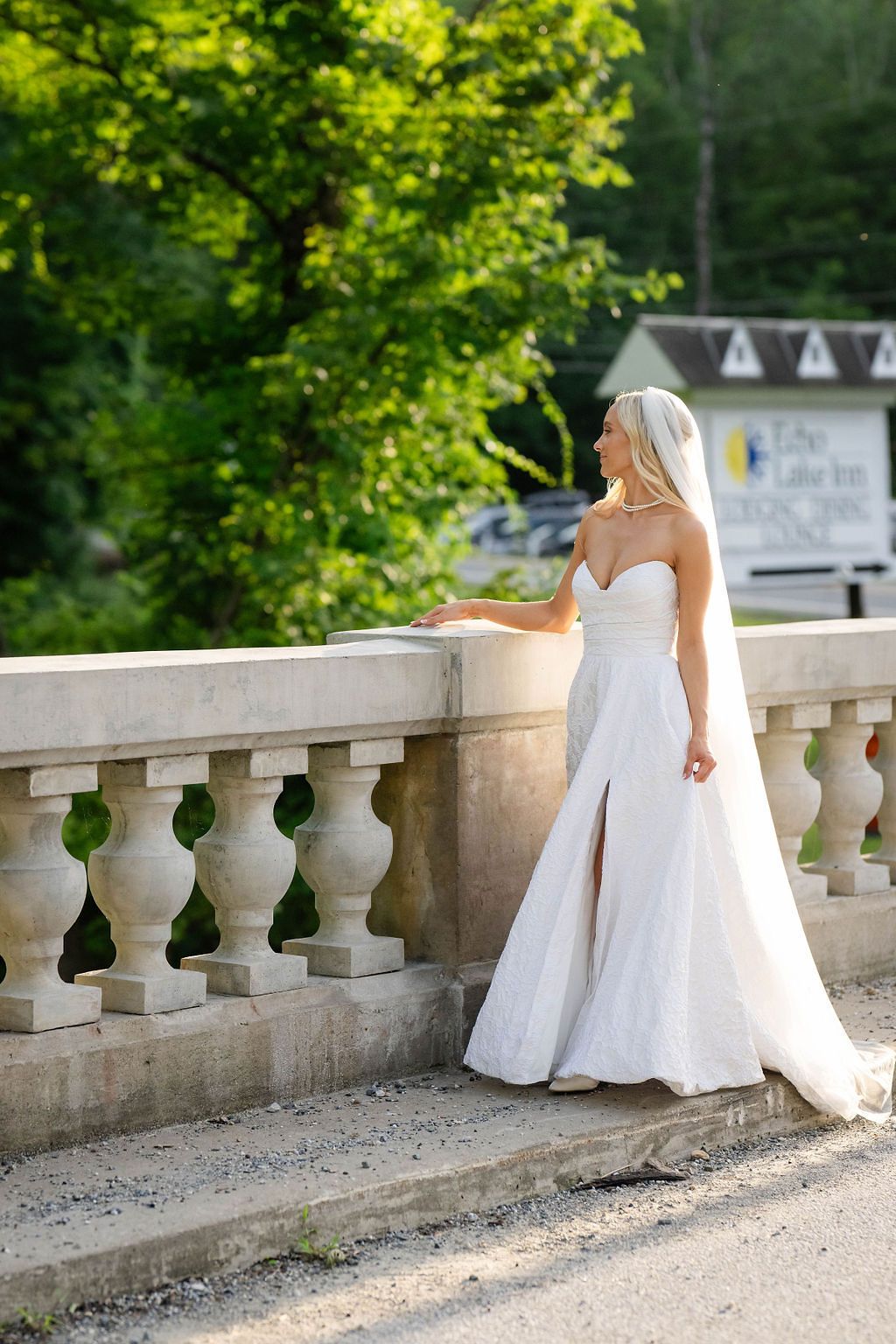 Elegant bride in strapless white gown and veil posing by a stone balustrade at Echo Lake Inn.