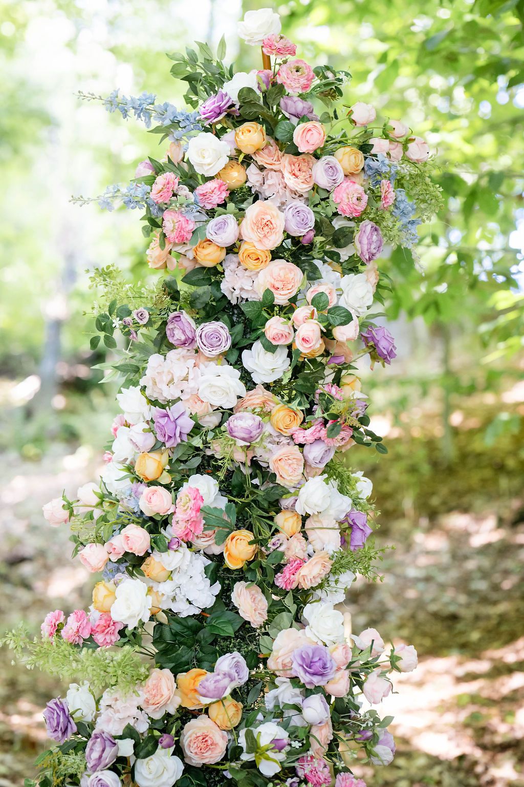 Elegant wedding arch decorated with colorful pastel roses in pink, purple, yellow, and white blooms outdoors.