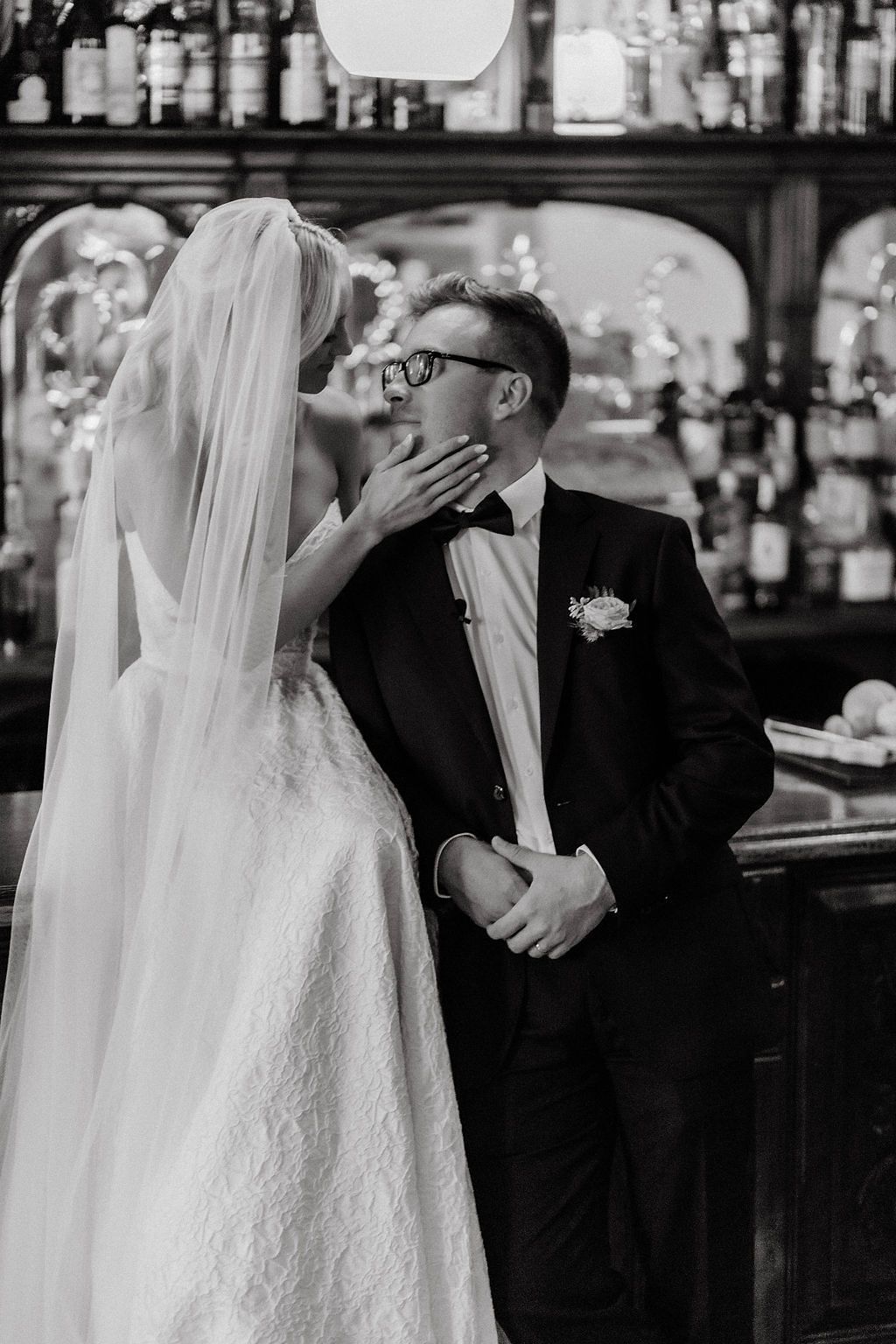 Black and white photo of bride and groom sharing tender kiss near elegant bar at wedding reception.