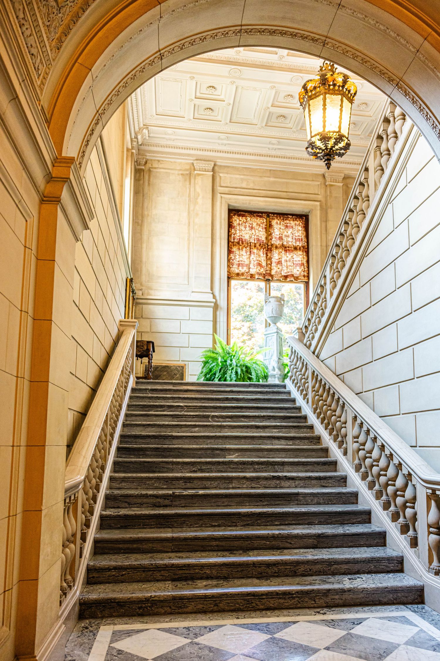 Elegant marble staircase with ornate balustrades, golden lantern, and arched ceiling in a classic grand interior building.