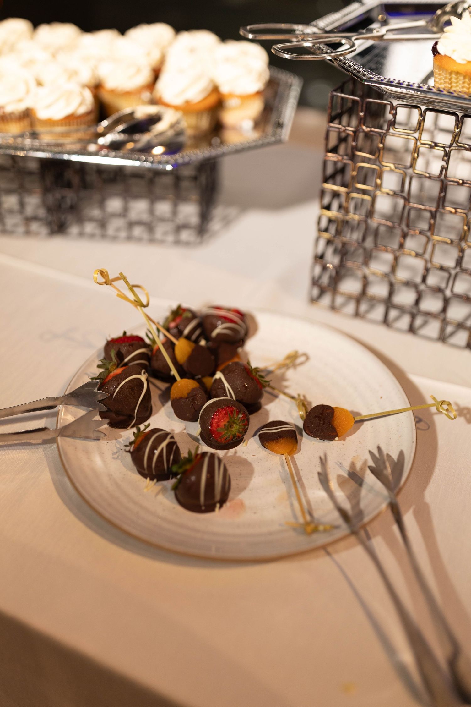 Elegant wedding dessert display featuring chocolate-dipped strawberries, truffles, and cupcakes on a white marble table.