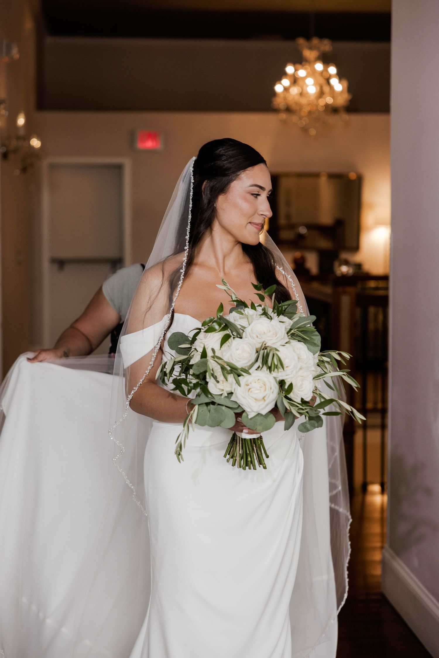Bride in white gown holding bouquet of white roses with veil.