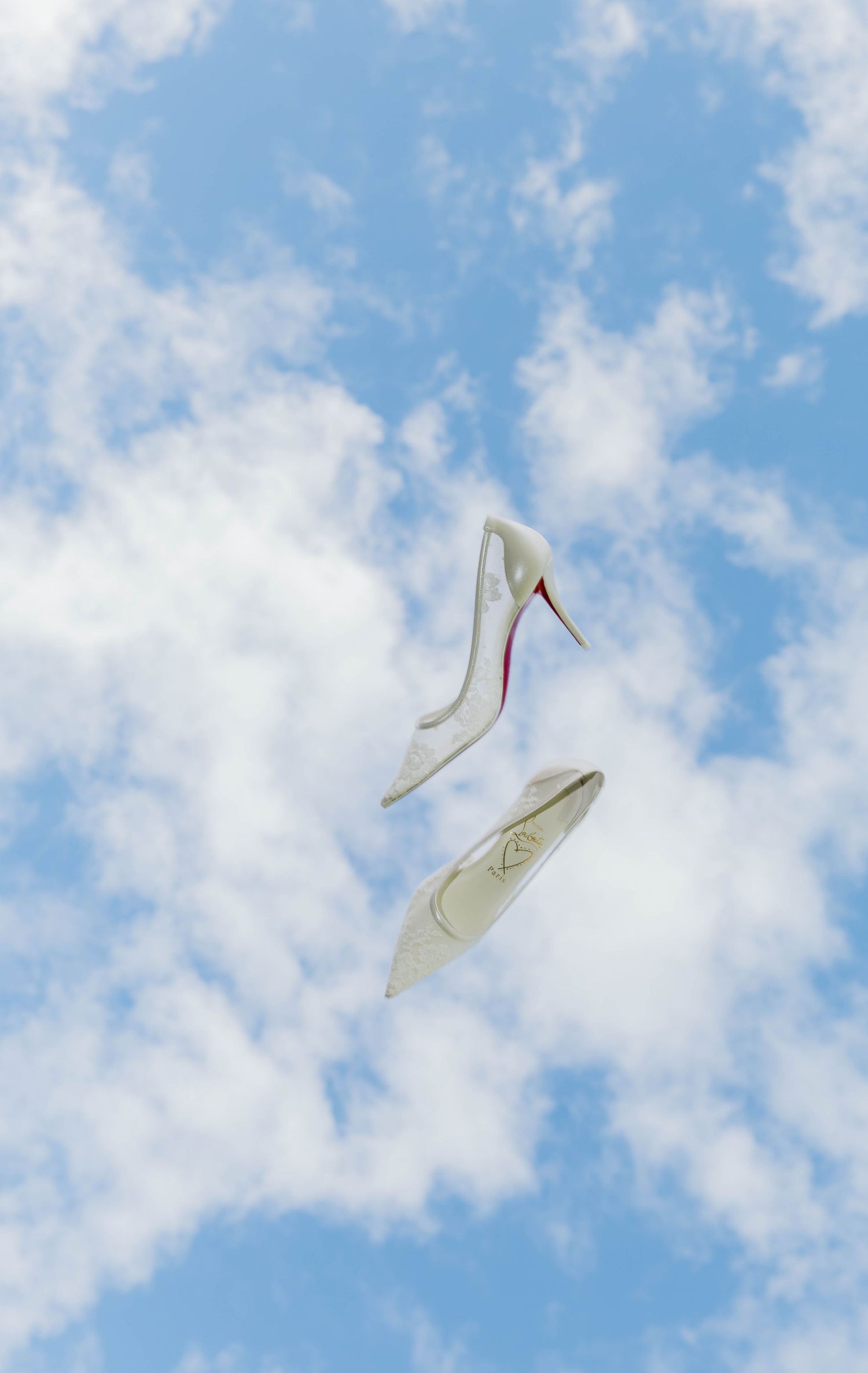 Two white high heel shoes floating against a blue sky with white clouds.