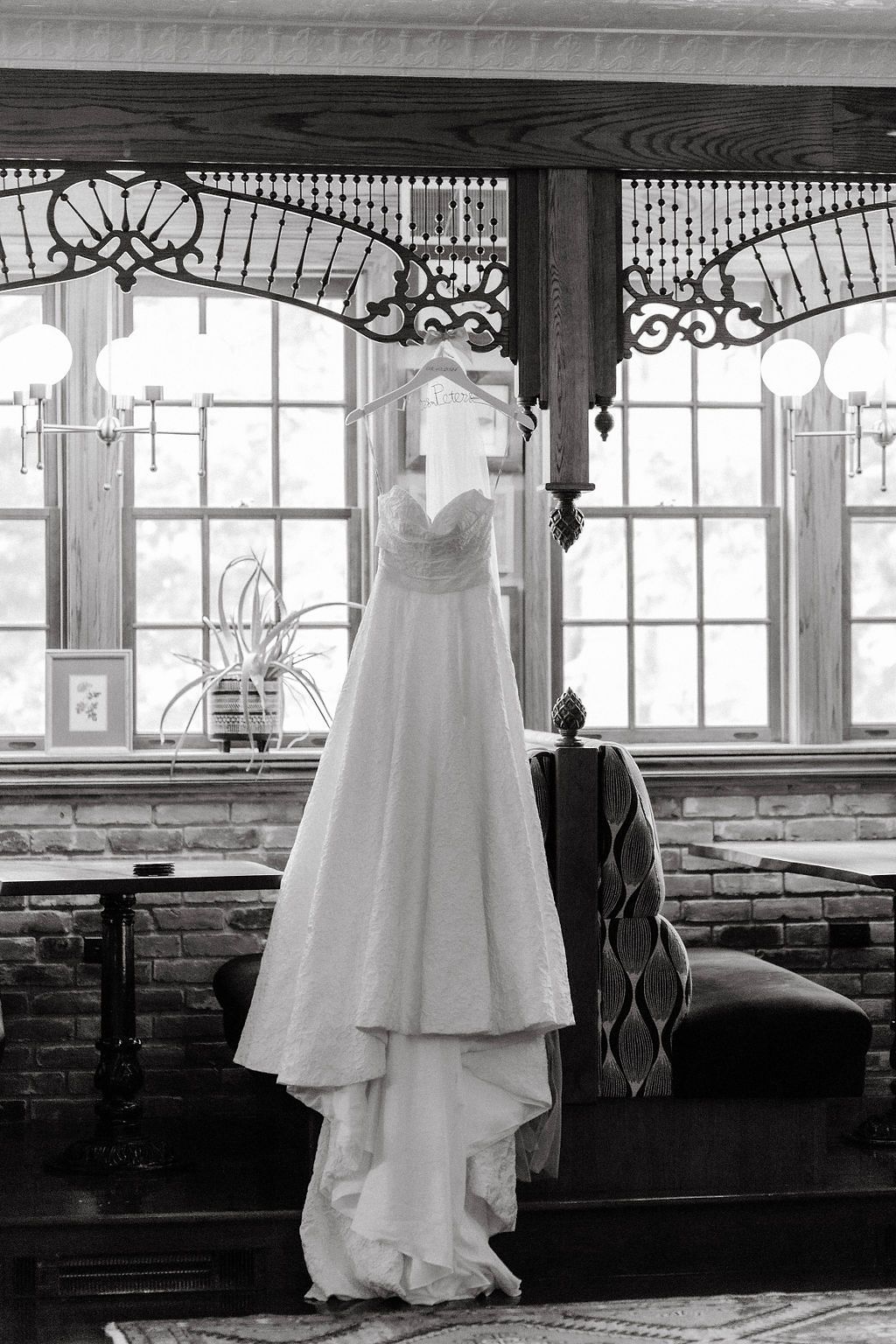 Black and white photo of a wedding gown hanging in a window of a vintage venue with ornate woodwork.