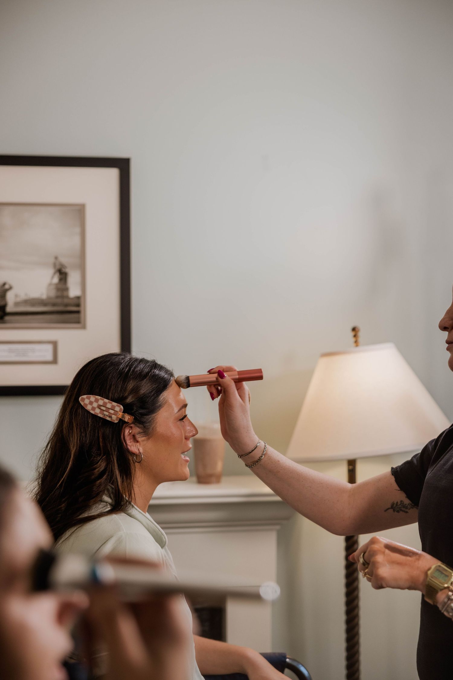 A makeup artist applying foundation to a smiling woman with a hair clip during a bridal getting-ready session.