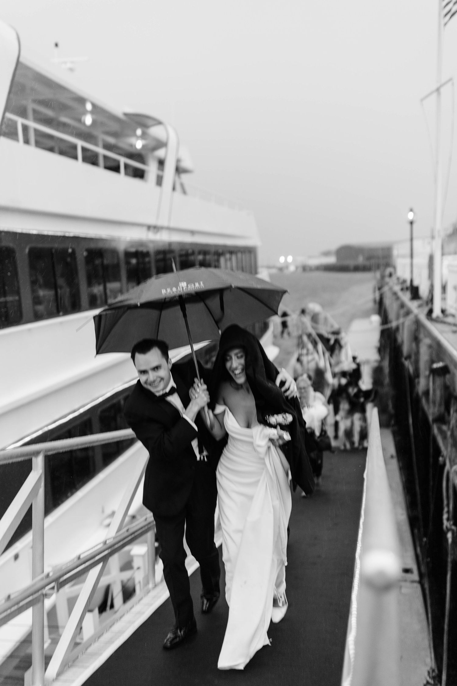 Bride and groom share a joyful moment under an umbrella on a rainy wedding day aboard a yacht.